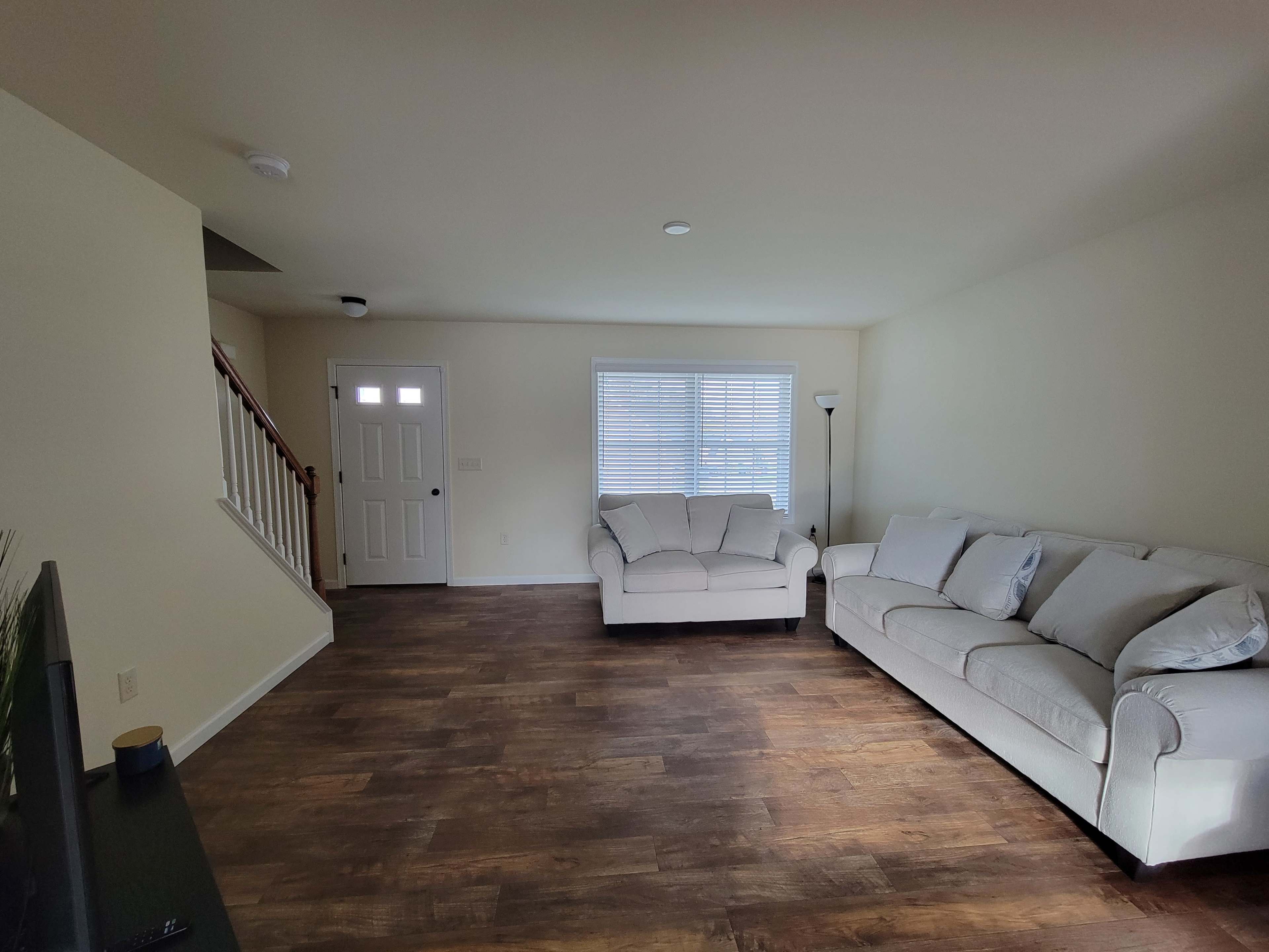 A light-colored living room with two sofas, a lamp, and a door leading outside, featuring wood flooring.