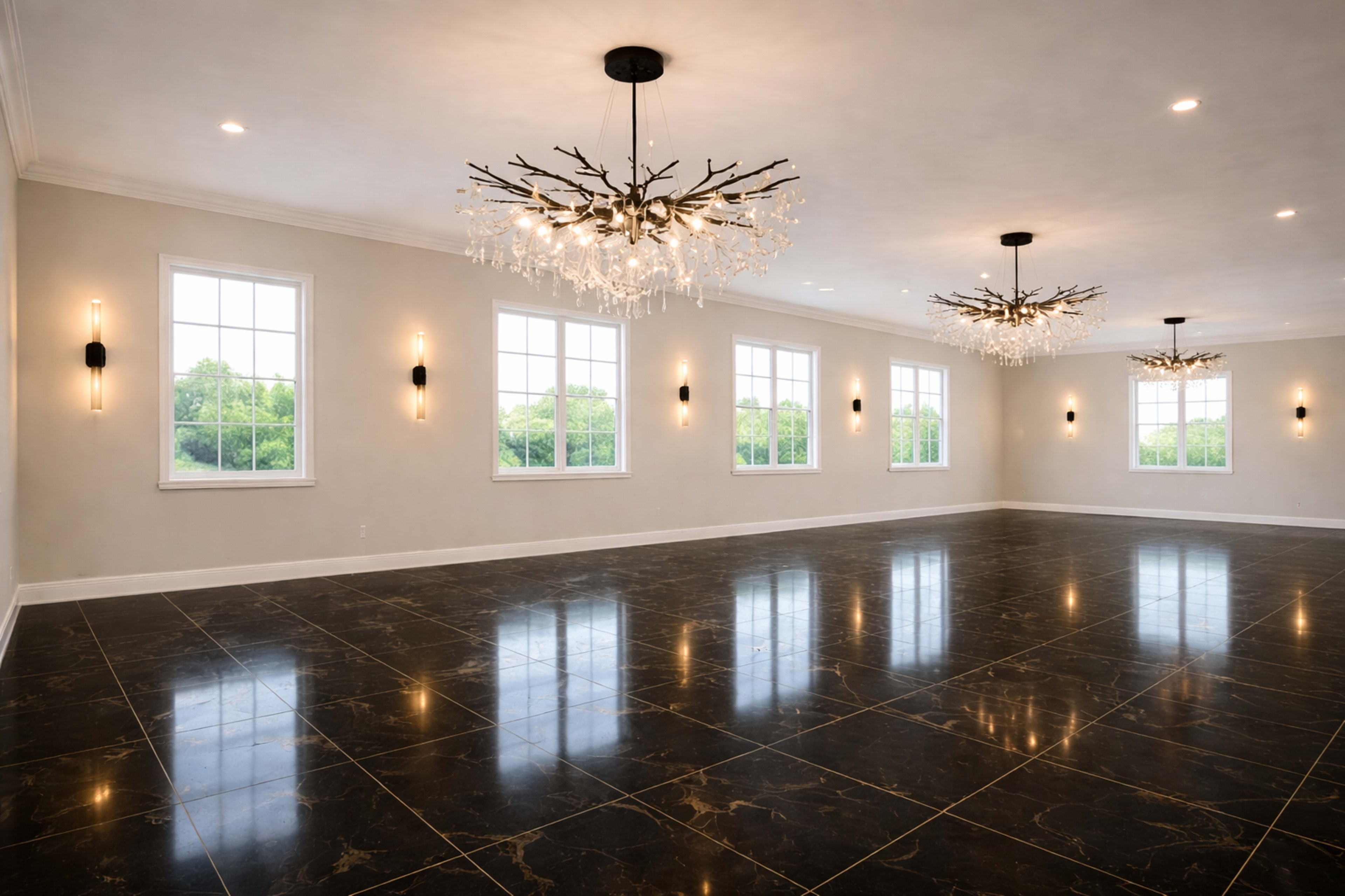 The image shows a spacious, well-lit room with large windows, a reflective black marble floor, and elegant chandeliers on the ceiling.