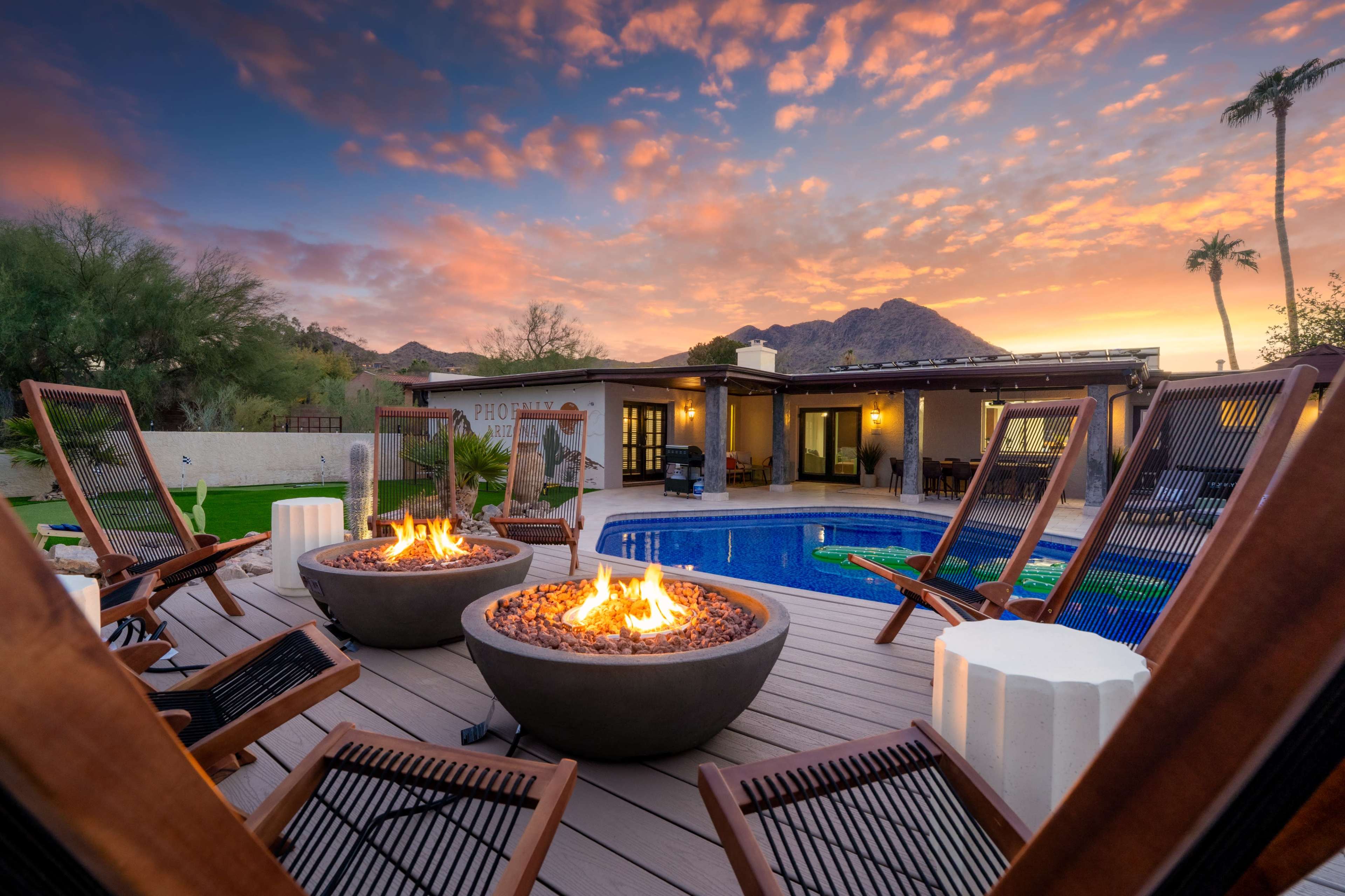 The image shows a backyard pool area with two fire pits, lounge chairs, and a backdrop of mountains under a colorful sunset sky.