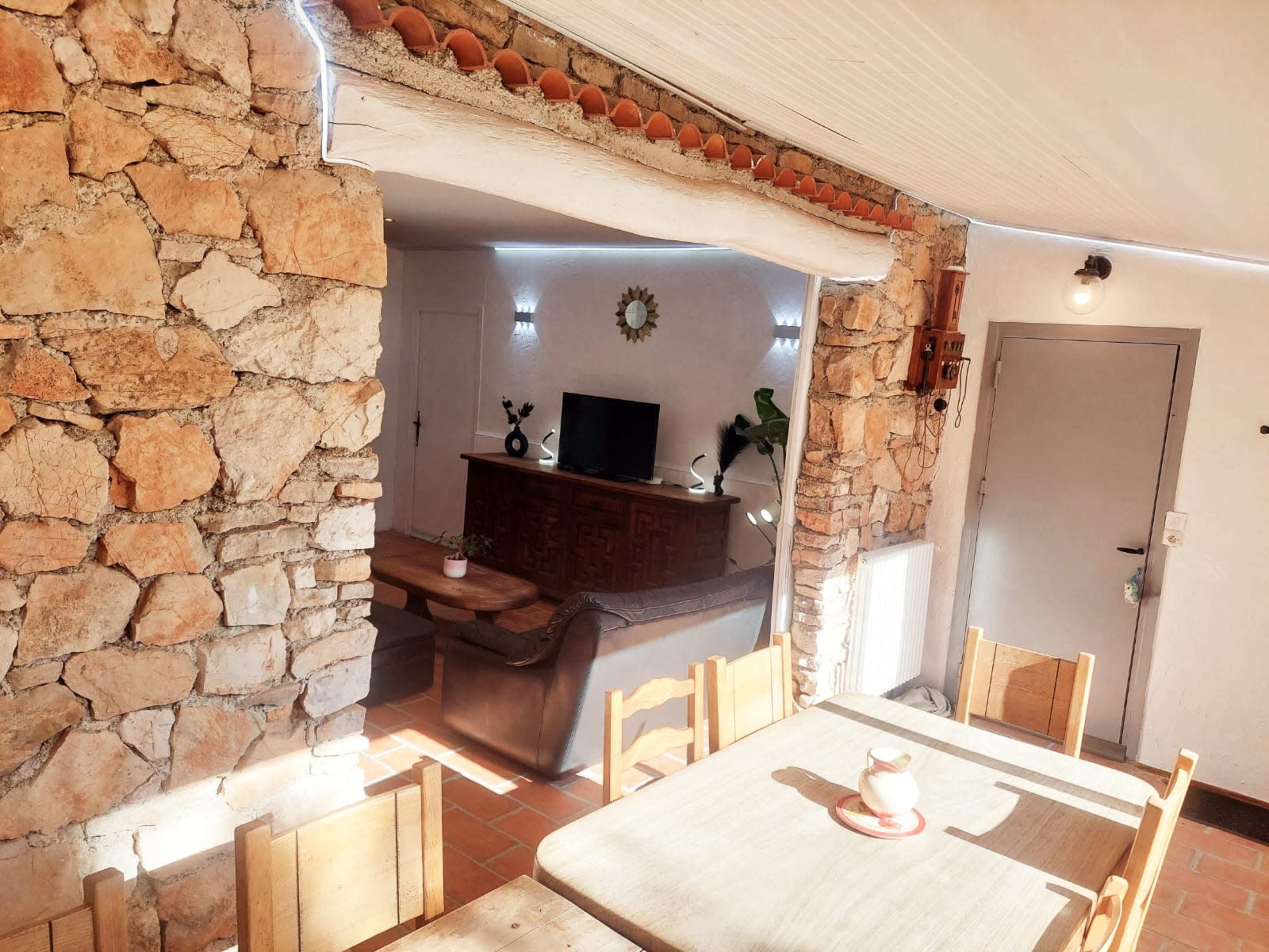 The image shows a living space with stone walls, a wooden dining table, a leather sofa, and a television in the background.