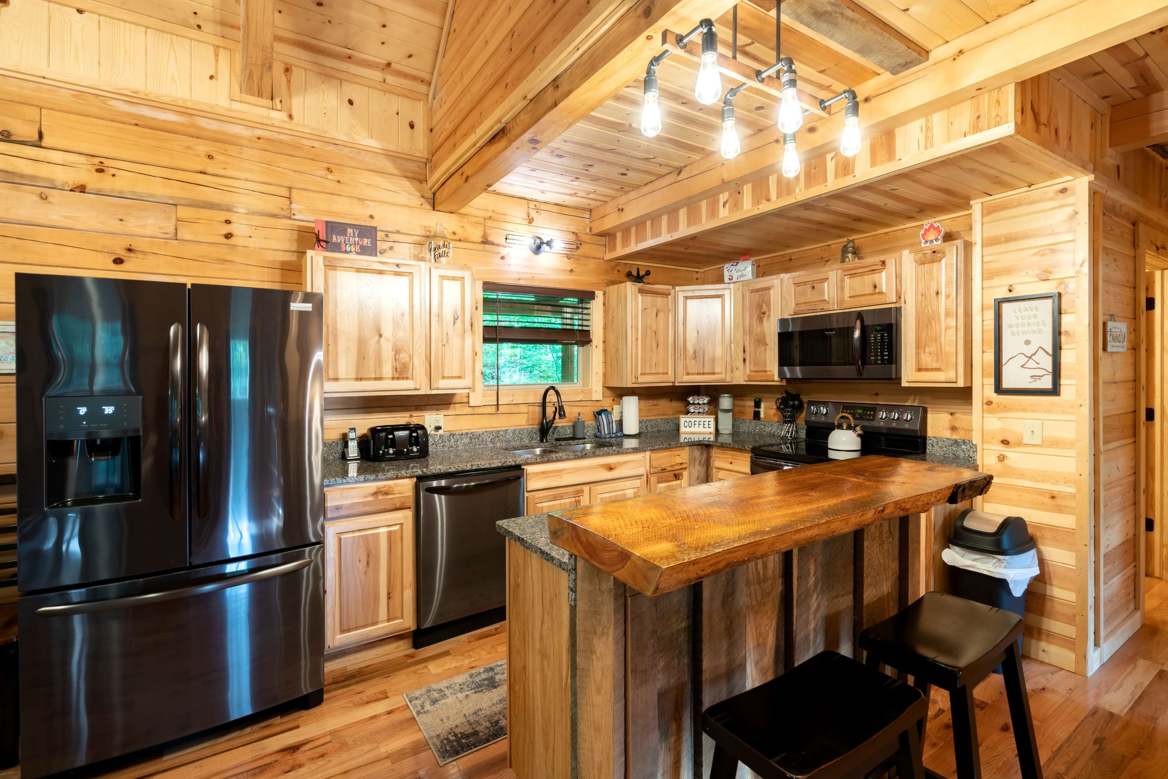A modern kitchen features wooden cabinets, a granite countertop, and stainless steel appliances, illuminated by pendant lights.