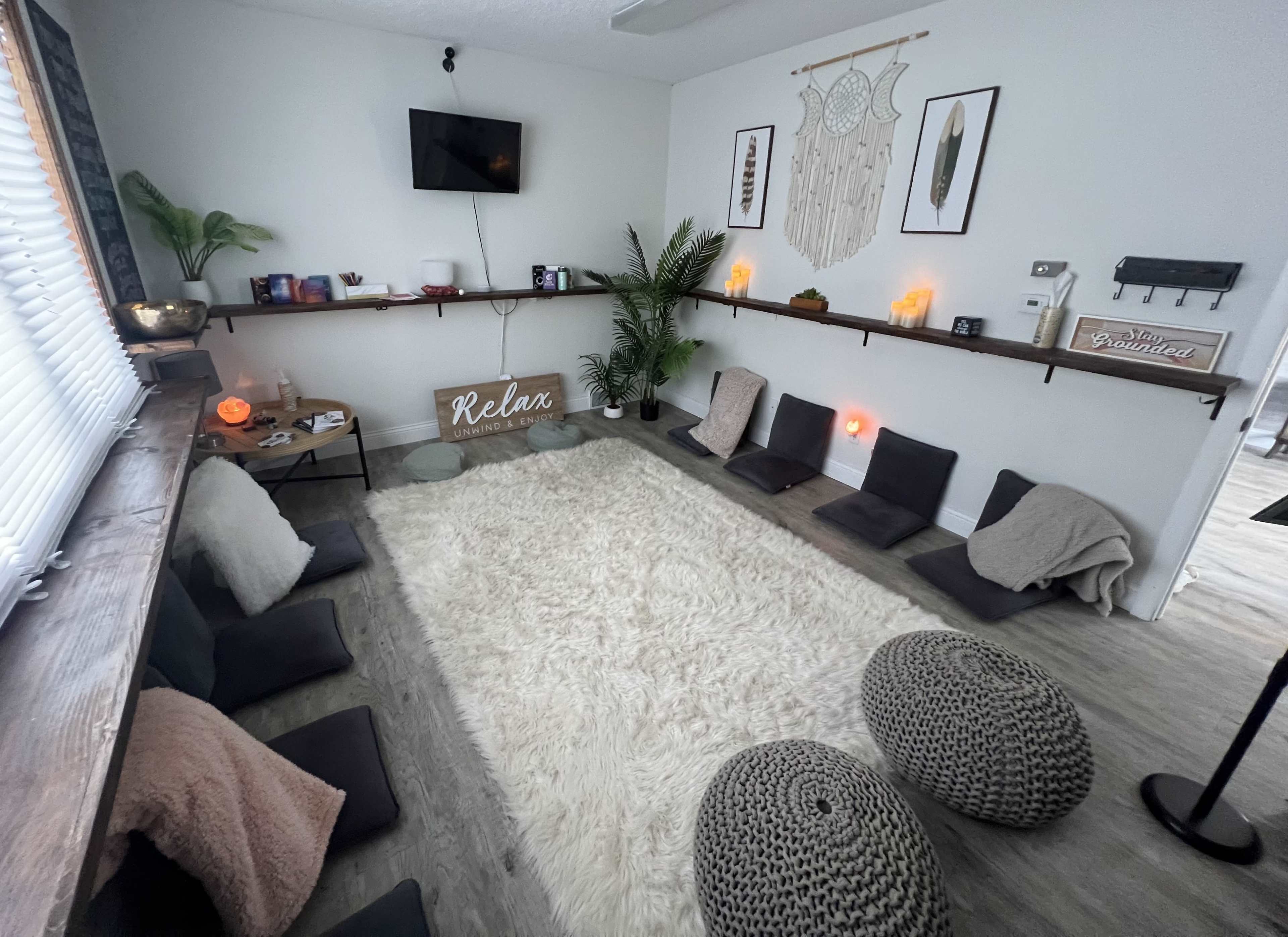 A tranquil relaxation room features a plush white rug, floor cushions, and decorative wall art, creating a serene environment.