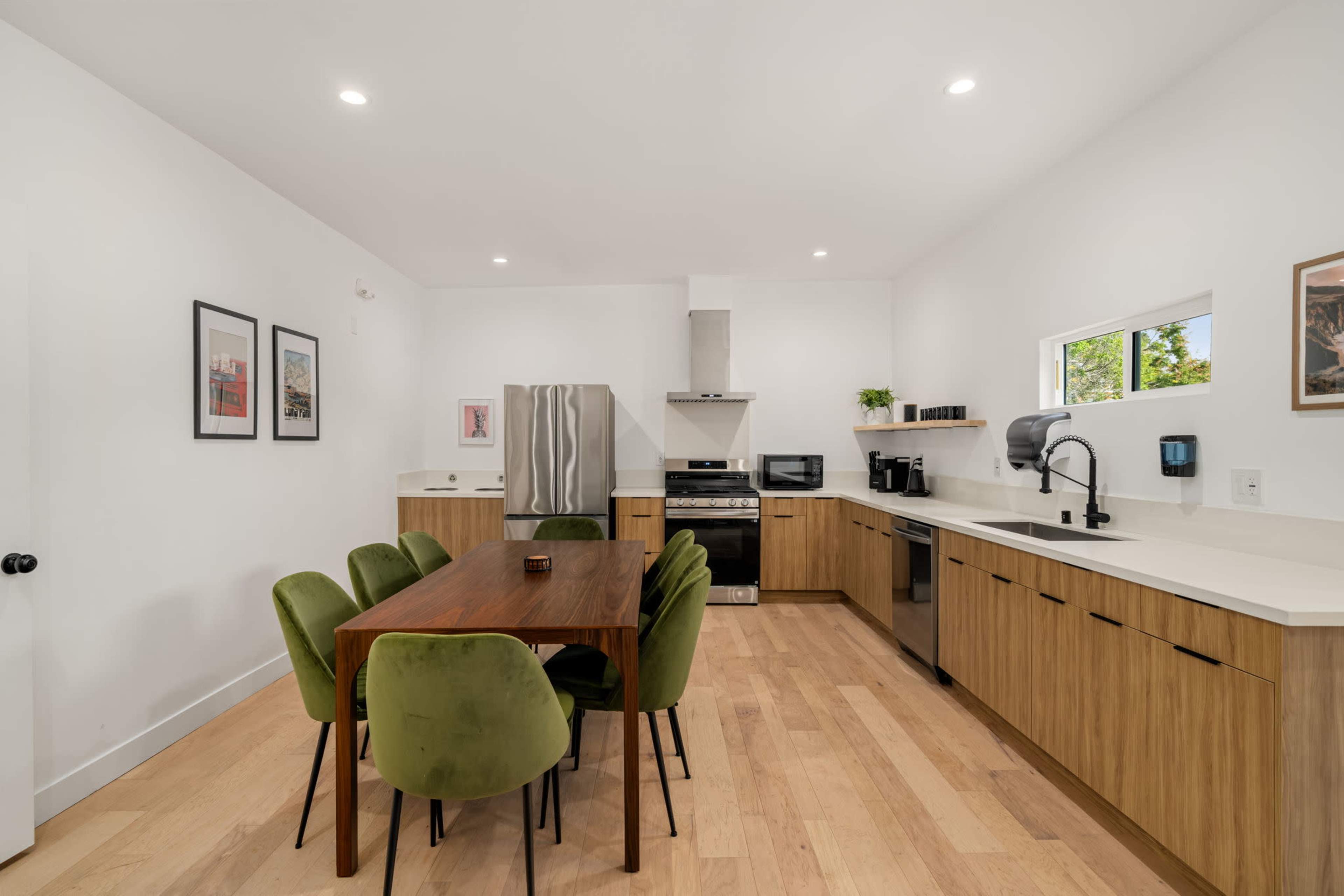 A modern kitchen features a wooden dining table surrounded by green chairs, with stainless steel appliances and a minimalist design.