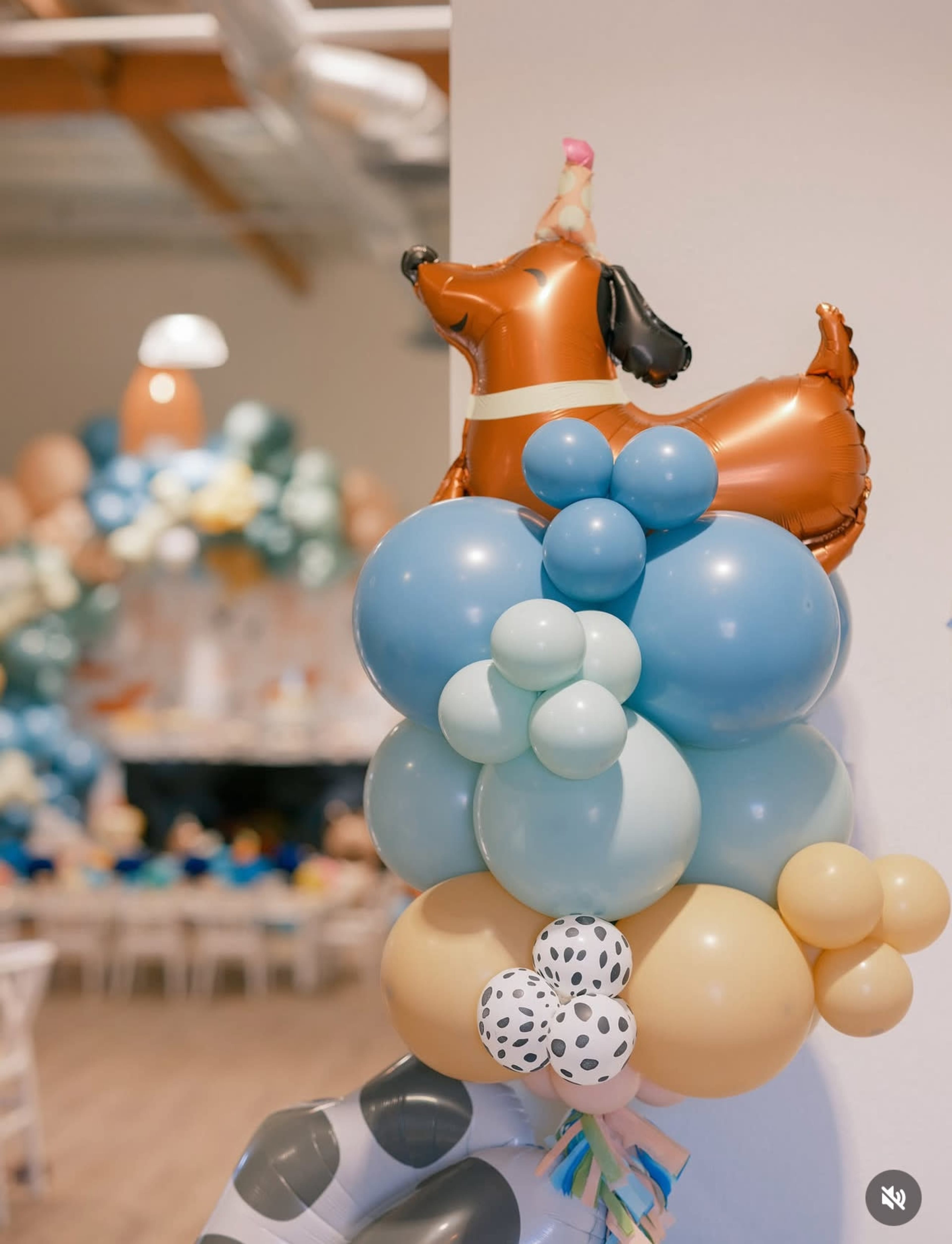 A decorative arrangement of colorful balloons, including a dog-shaped balloon, is displayed against a wall in a party setting.