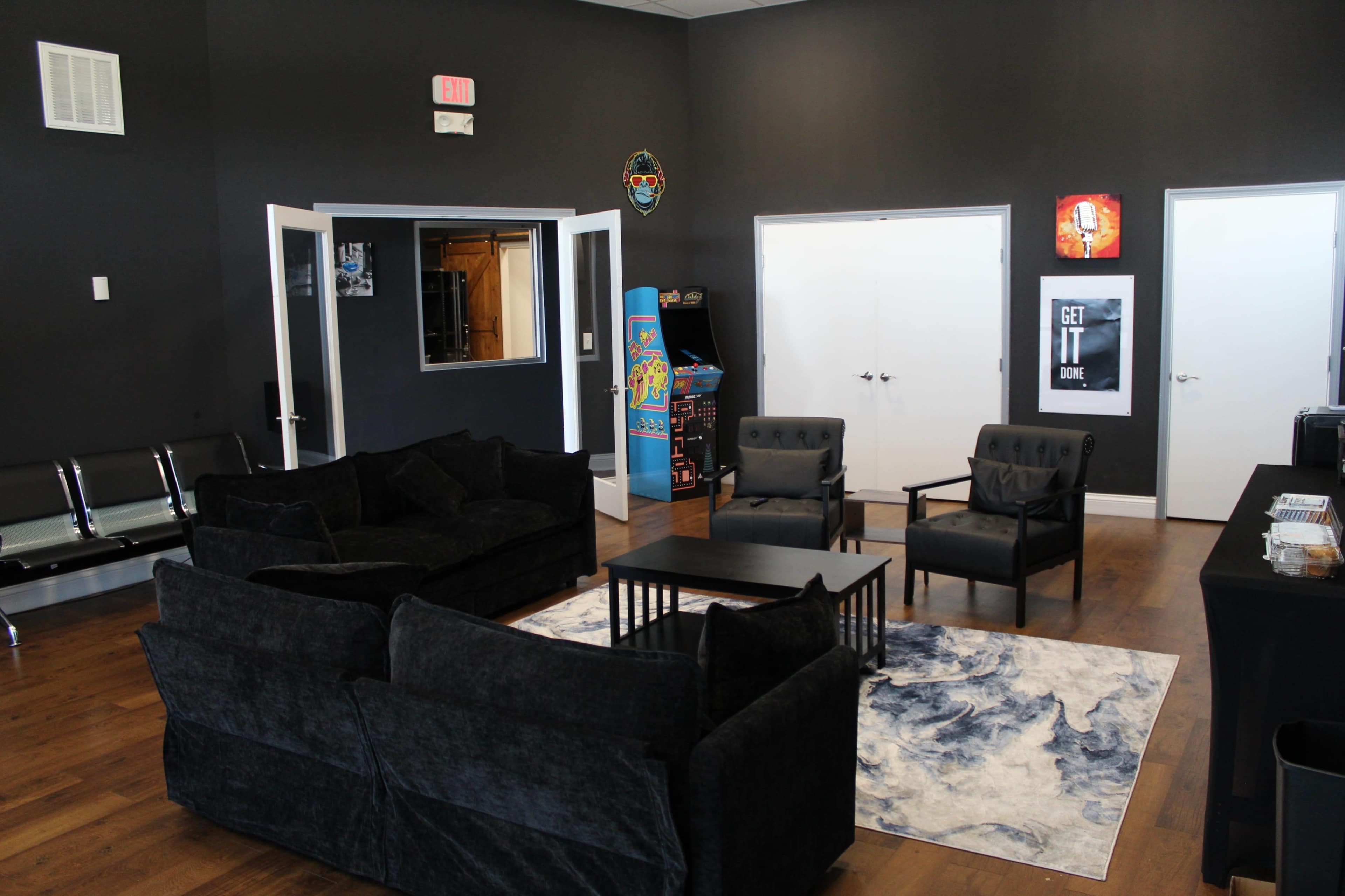 The image shows a modern lounge area with dark walls, a black carpet, a coffee table, and several seating arrangements, including black sofas and armchairs.