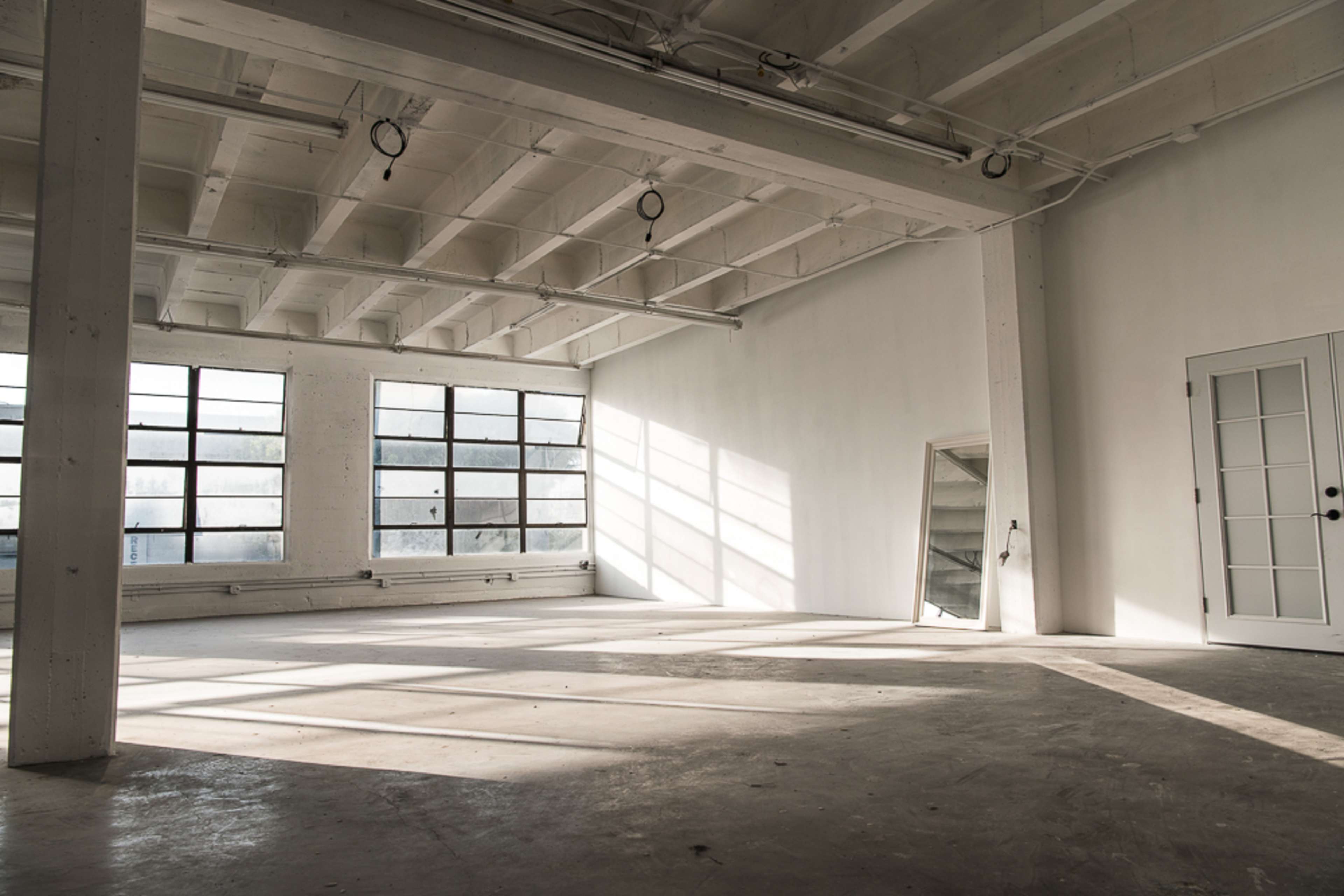 A spacious, empty room with large windows allowing light to cast shadows on the concrete floor.