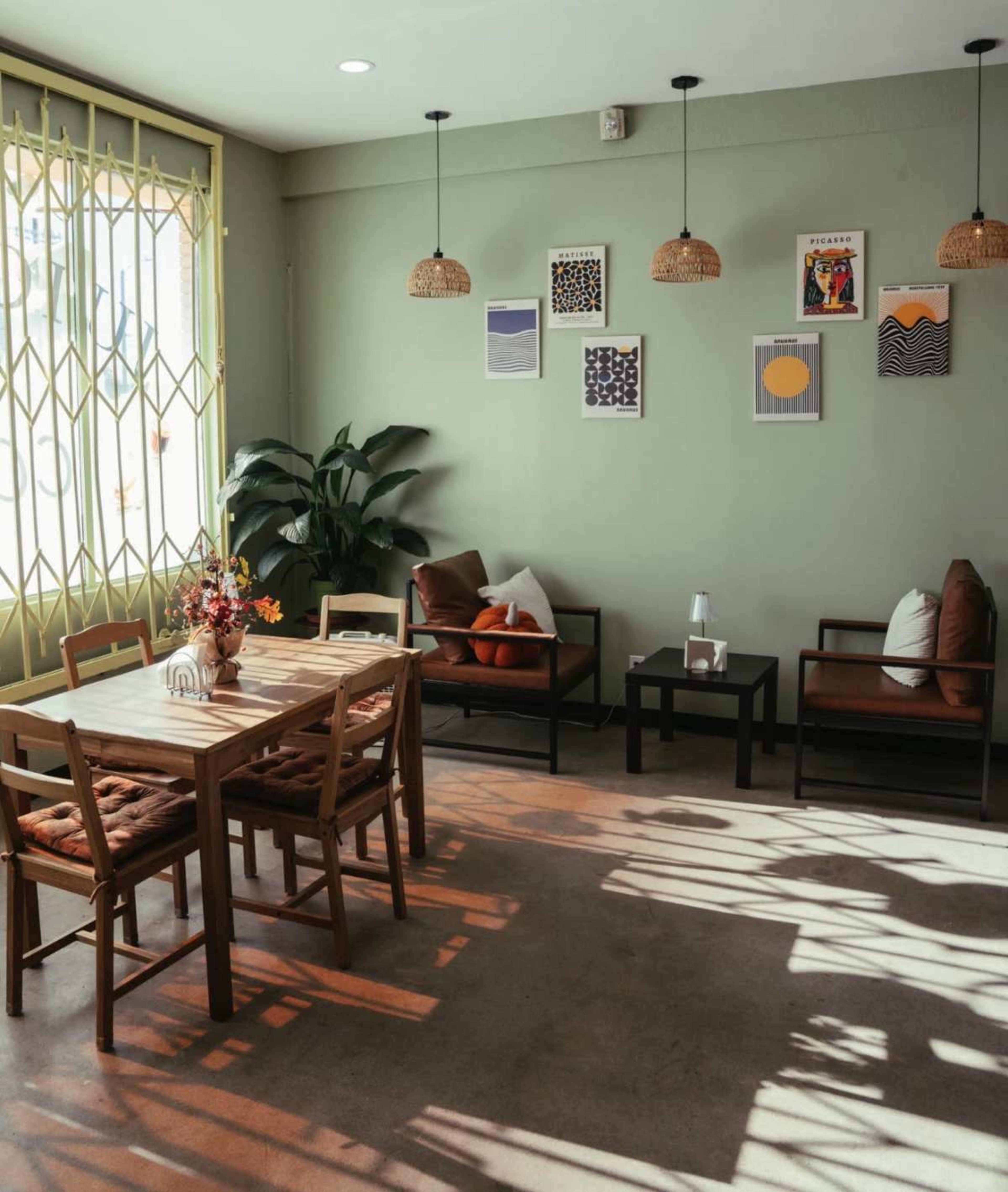 The image shows a bright interior of a cozy café with wooden furniture, green walls, and framed art displayed on the wall.