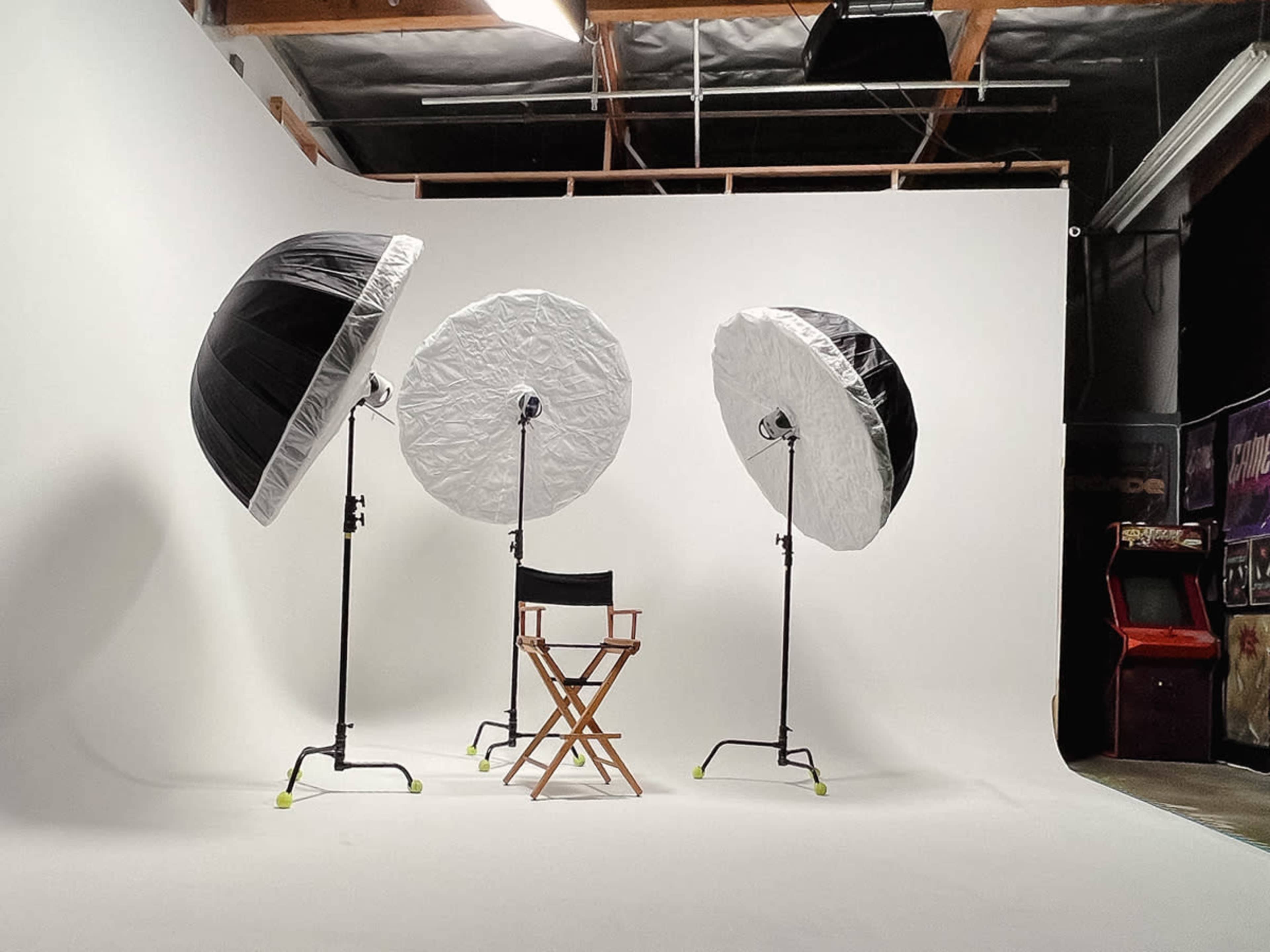 A photography studio setup with three softbox lights and a director's chair against a white backdrop.