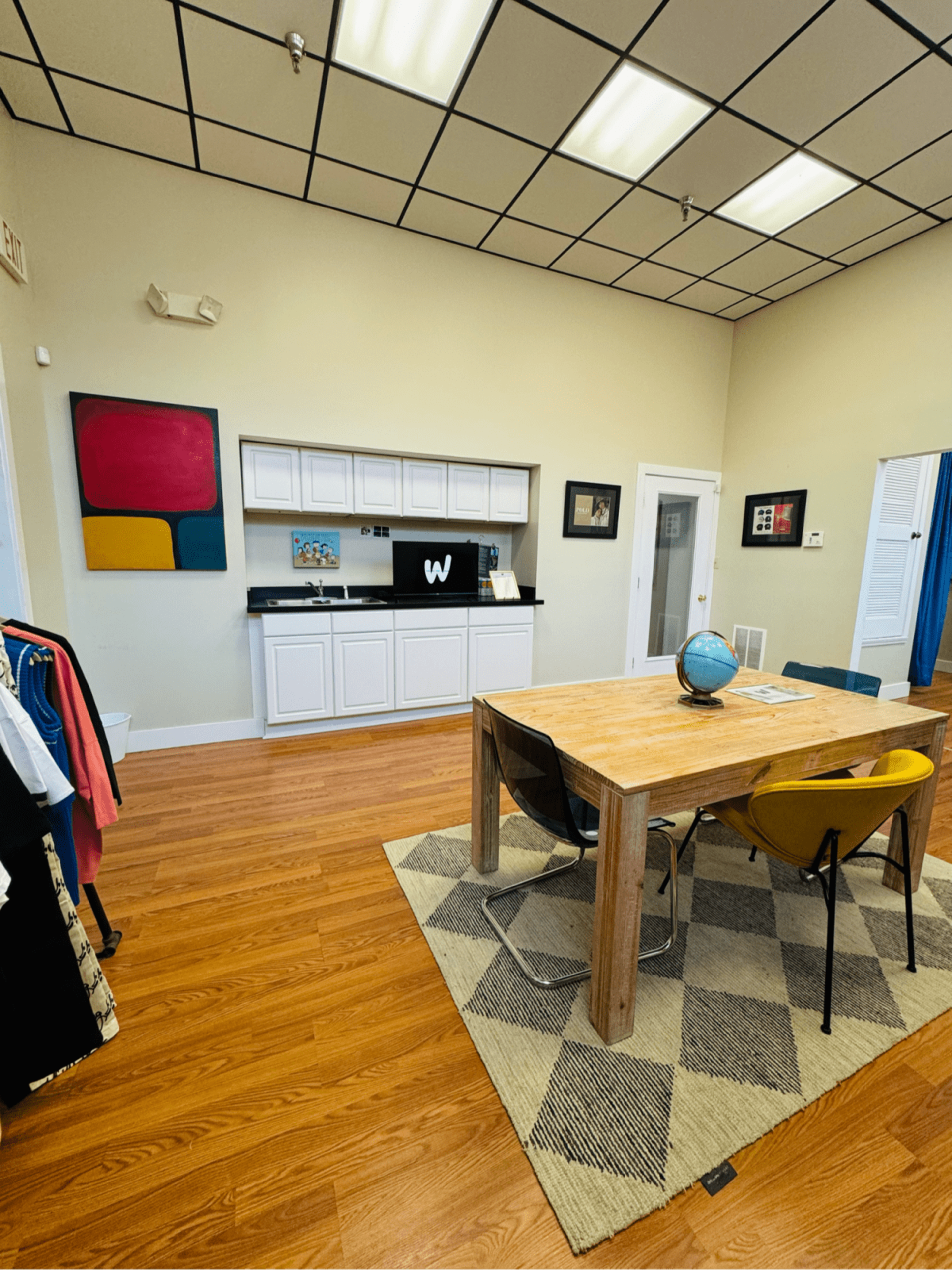 The image shows a modern meeting room with a wooden table and colorful chairs, featuring a black countertop setup and artwork on the walls.