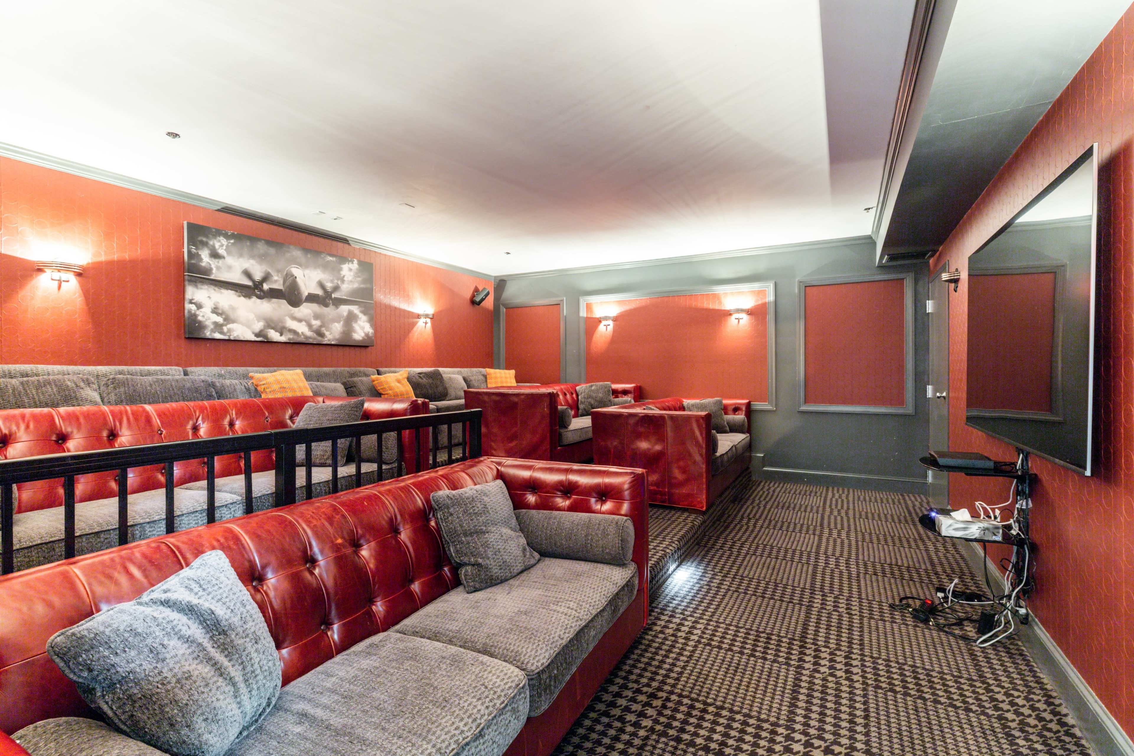 A home theater with red walls, plush seating arranged in tiers, and a large screen mounted on one wall.