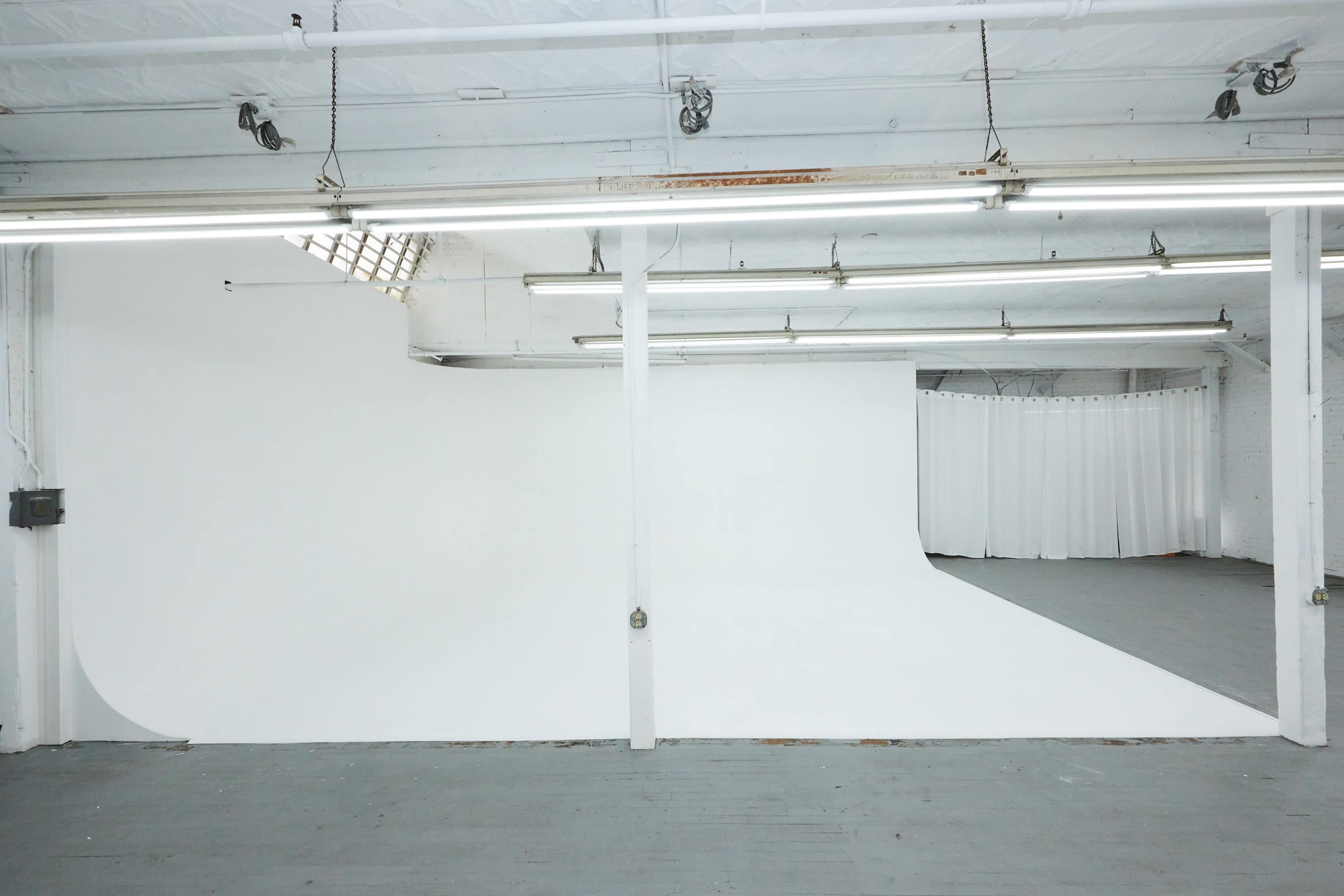 The image shows a spacious photo studio with a seamless white backdrop and gray flooring.