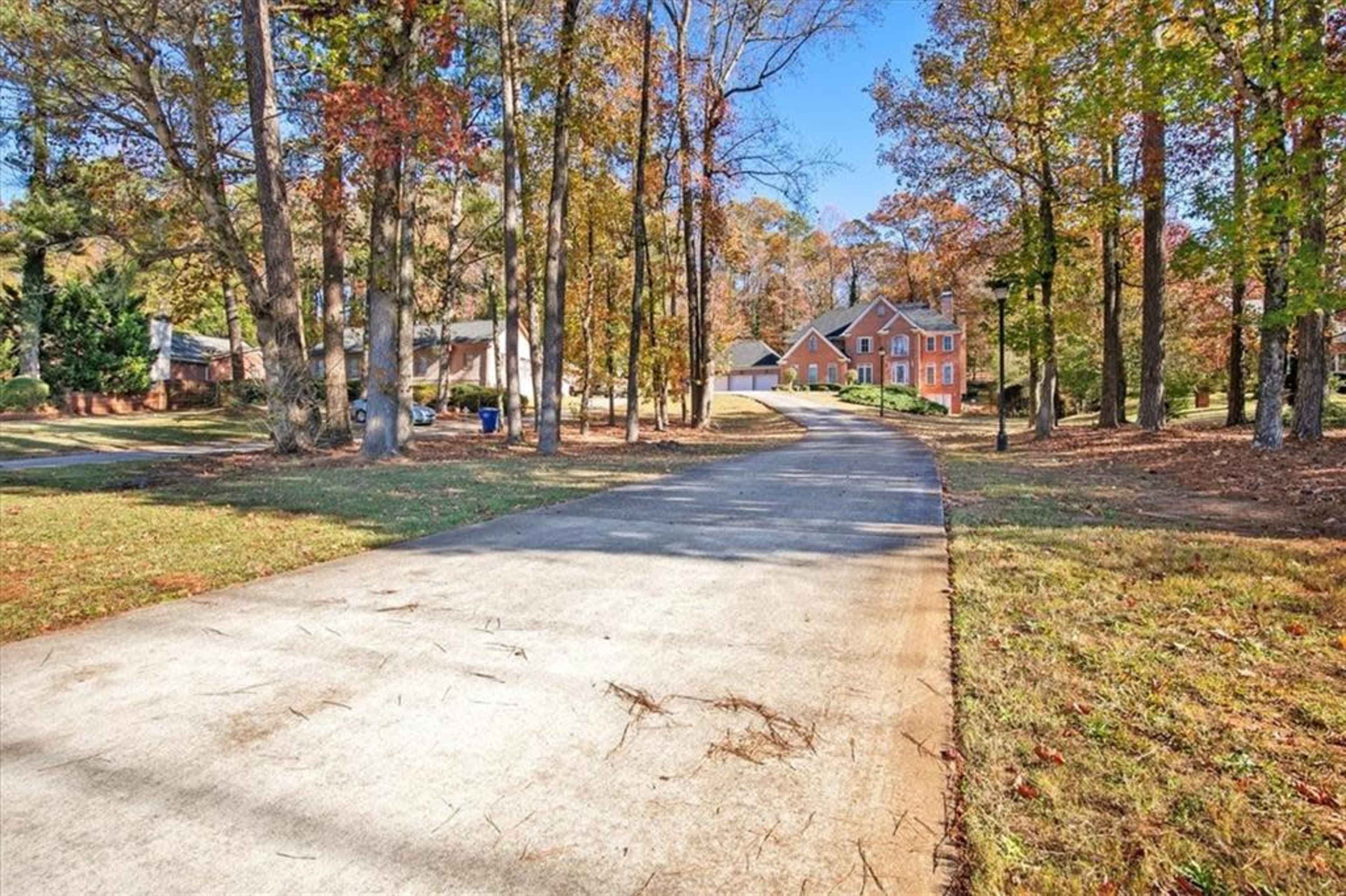A paved driveway leads through a wooded area to two houses, with one prominently visible on the right.