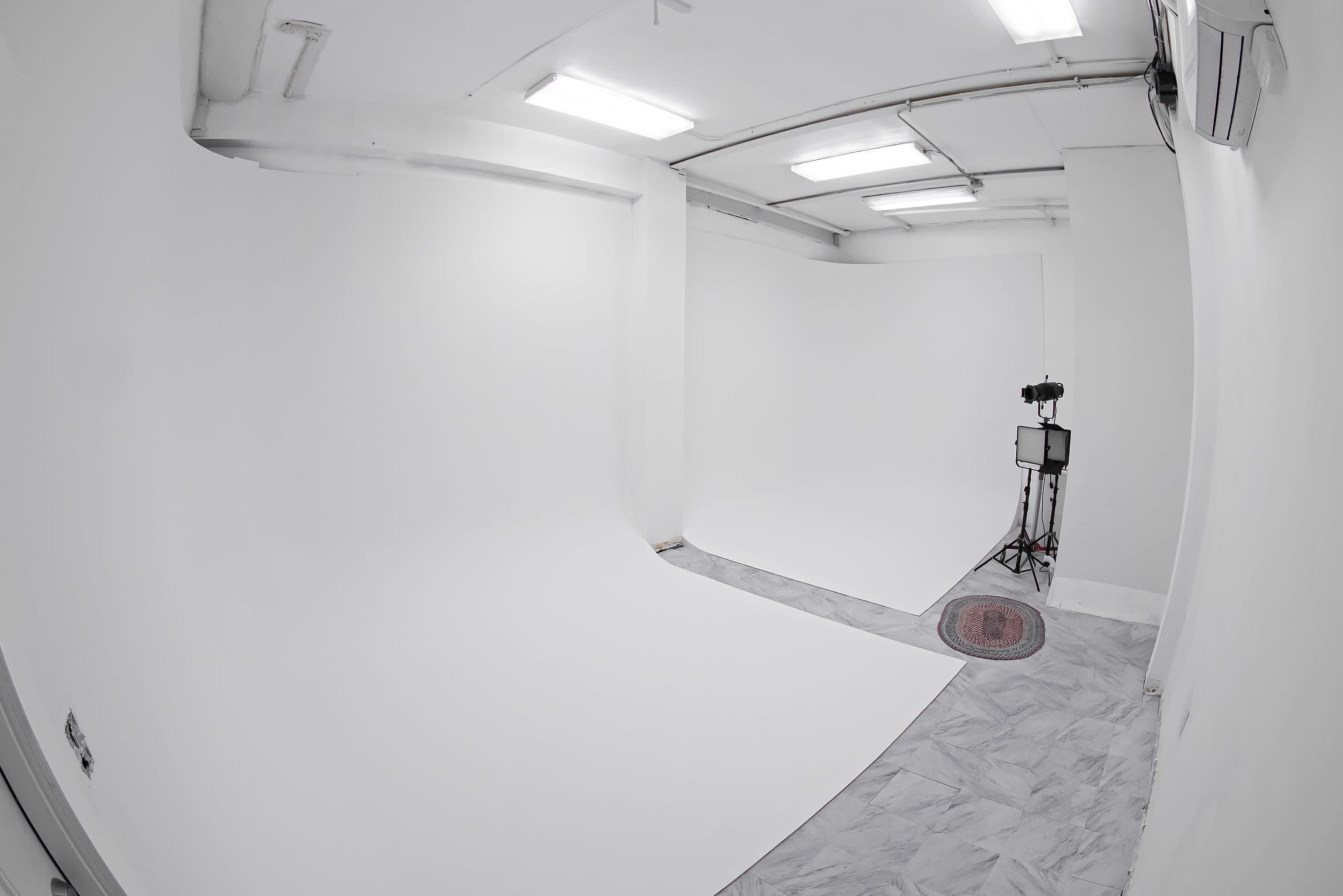 The image shows a spacious, empty photography studio with white walls and a seamless backdrop.