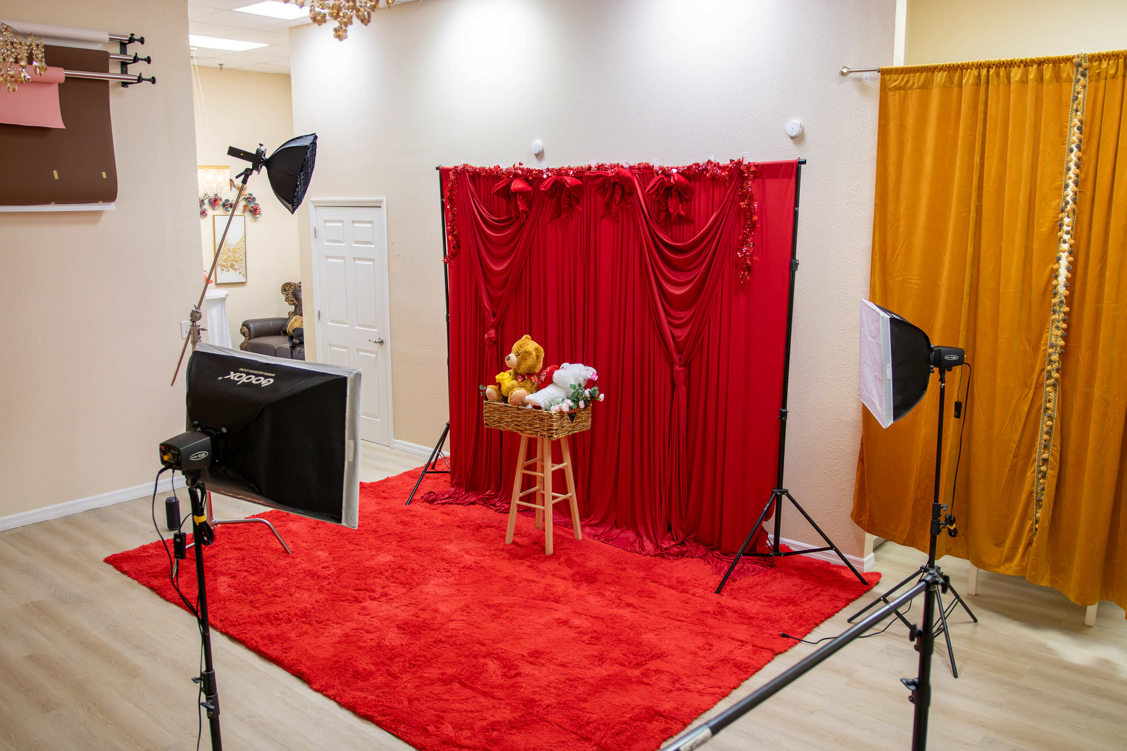 The image shows a photography studio setup with a red backdrop, a stool with props, and studio lights arranged around a red carpeted area.