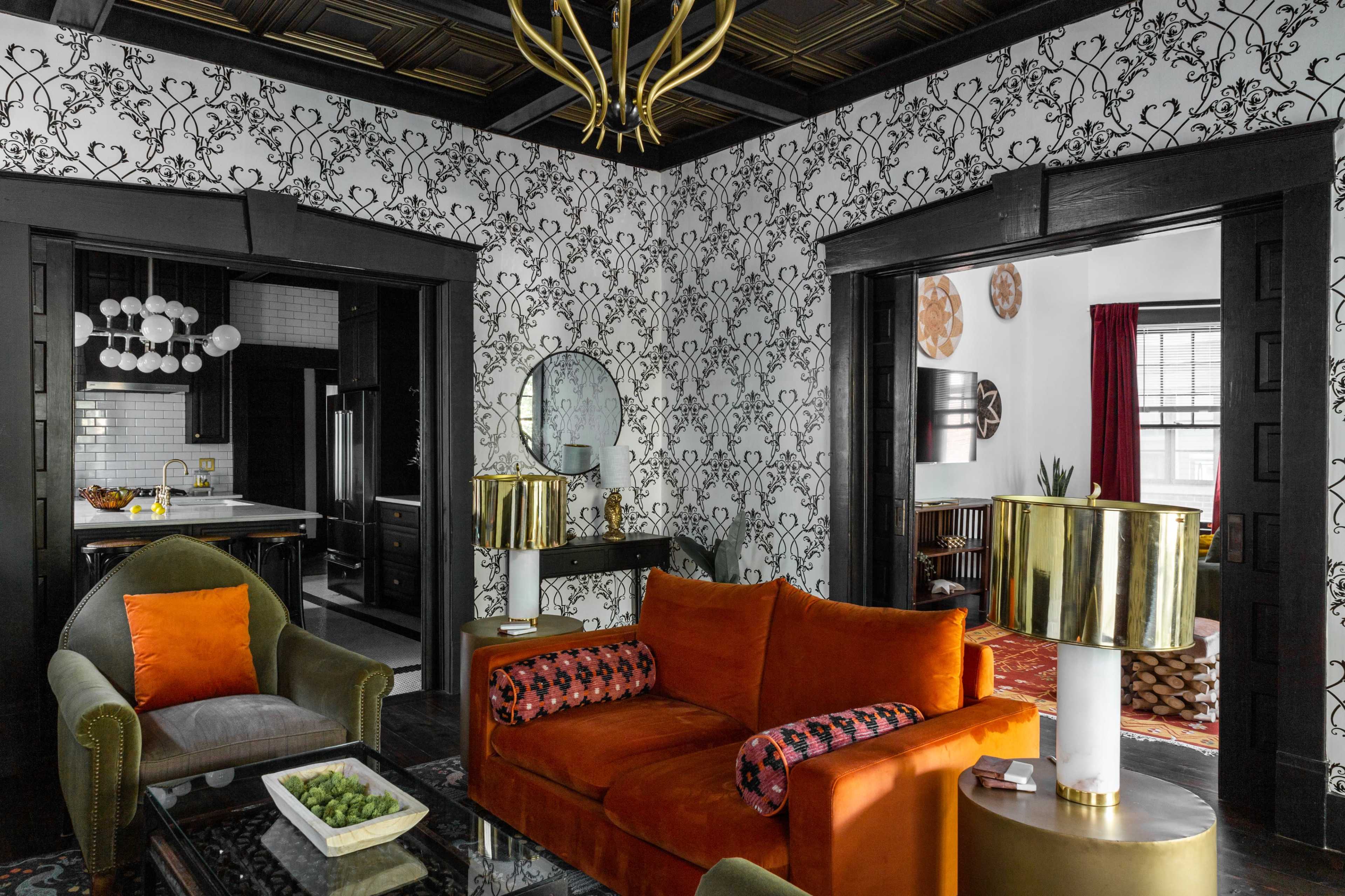 A stylish living room featuring a patterned wallpaper, a large orange sofa, and dark wooden trim.
