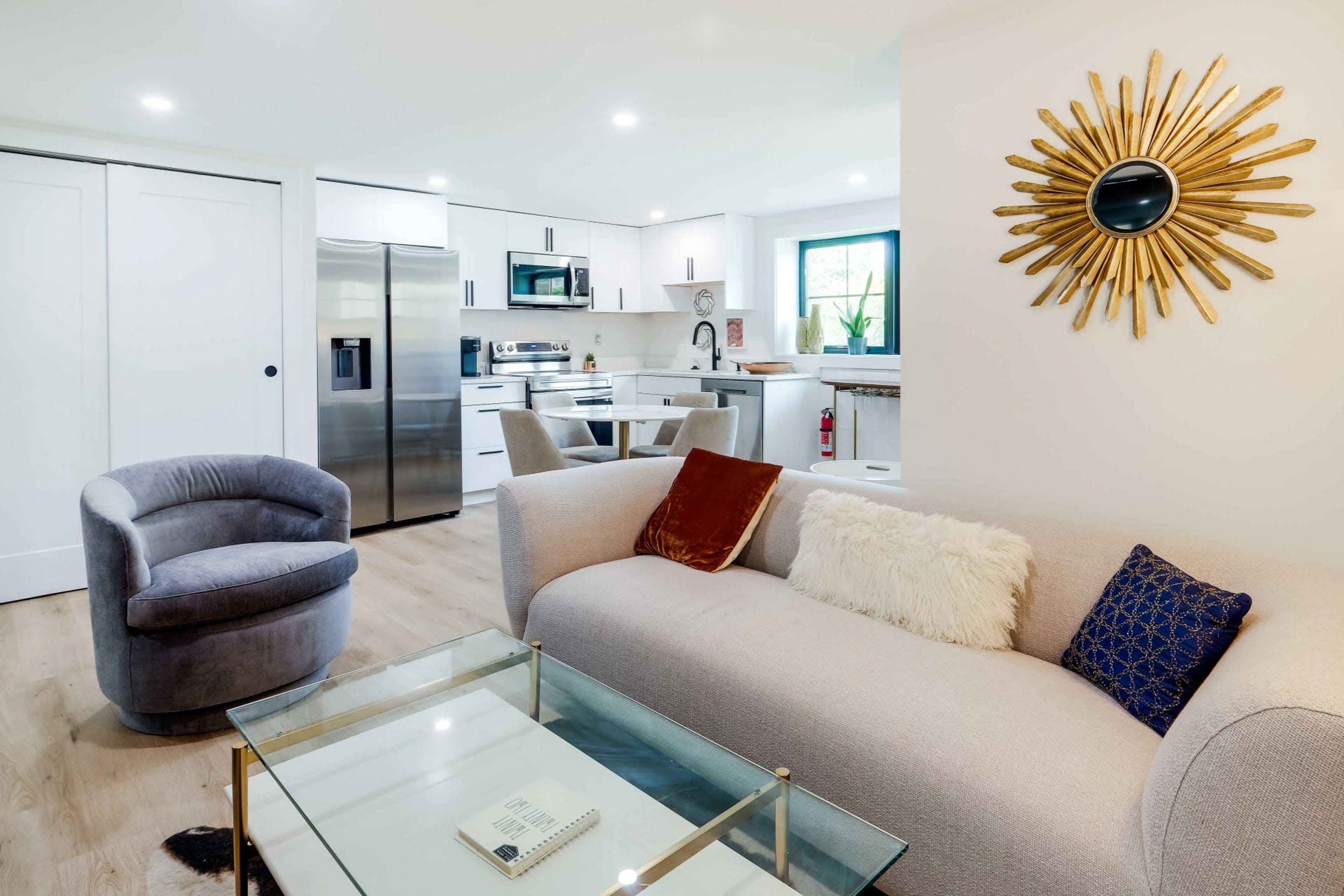 A modern living room with a light-colored sofa, a glass coffee table, and a view of a kitchen in the background.