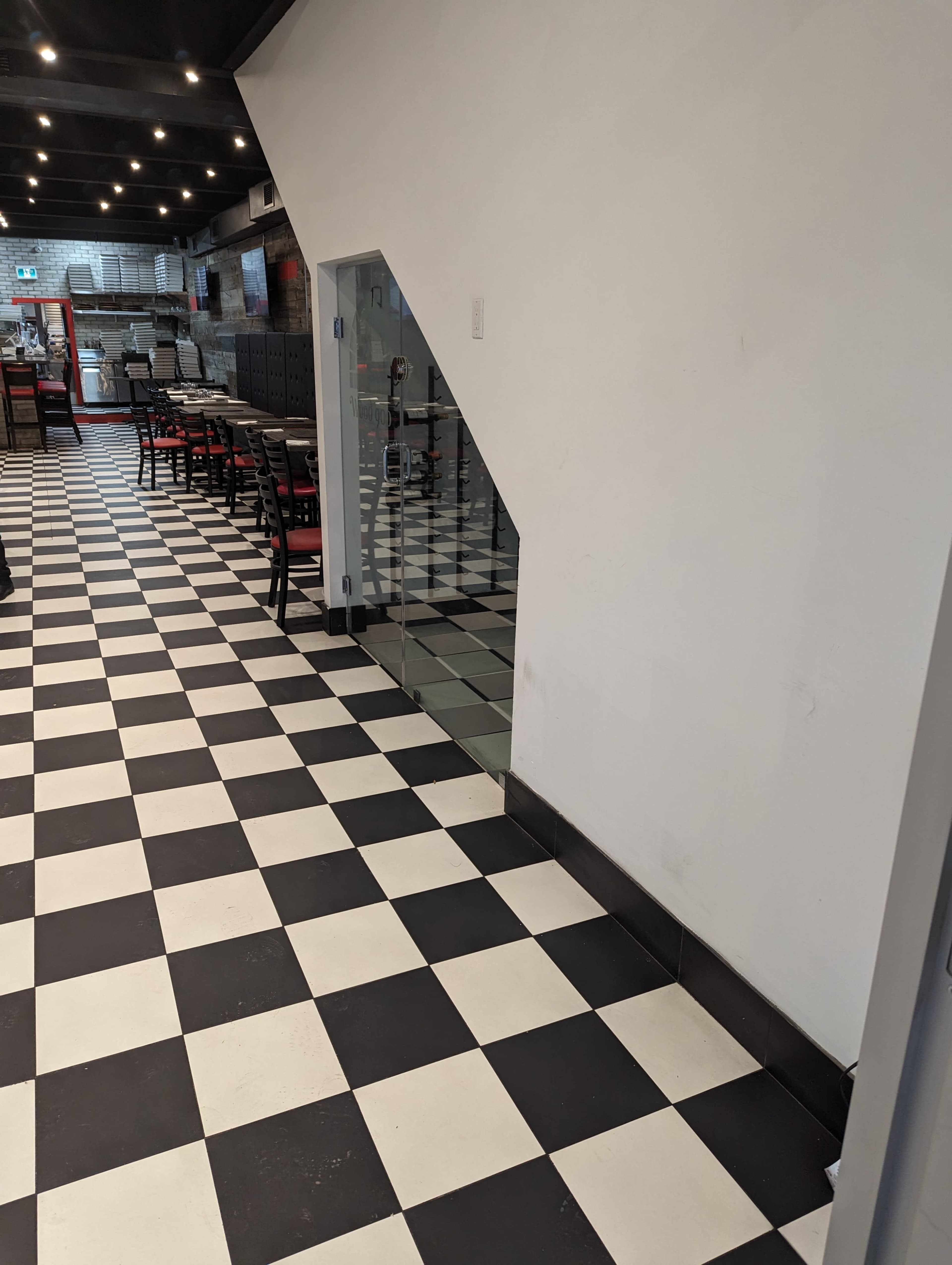 A black and white checkered floor in a restaurant hallway leading to a glass wall and seating area.