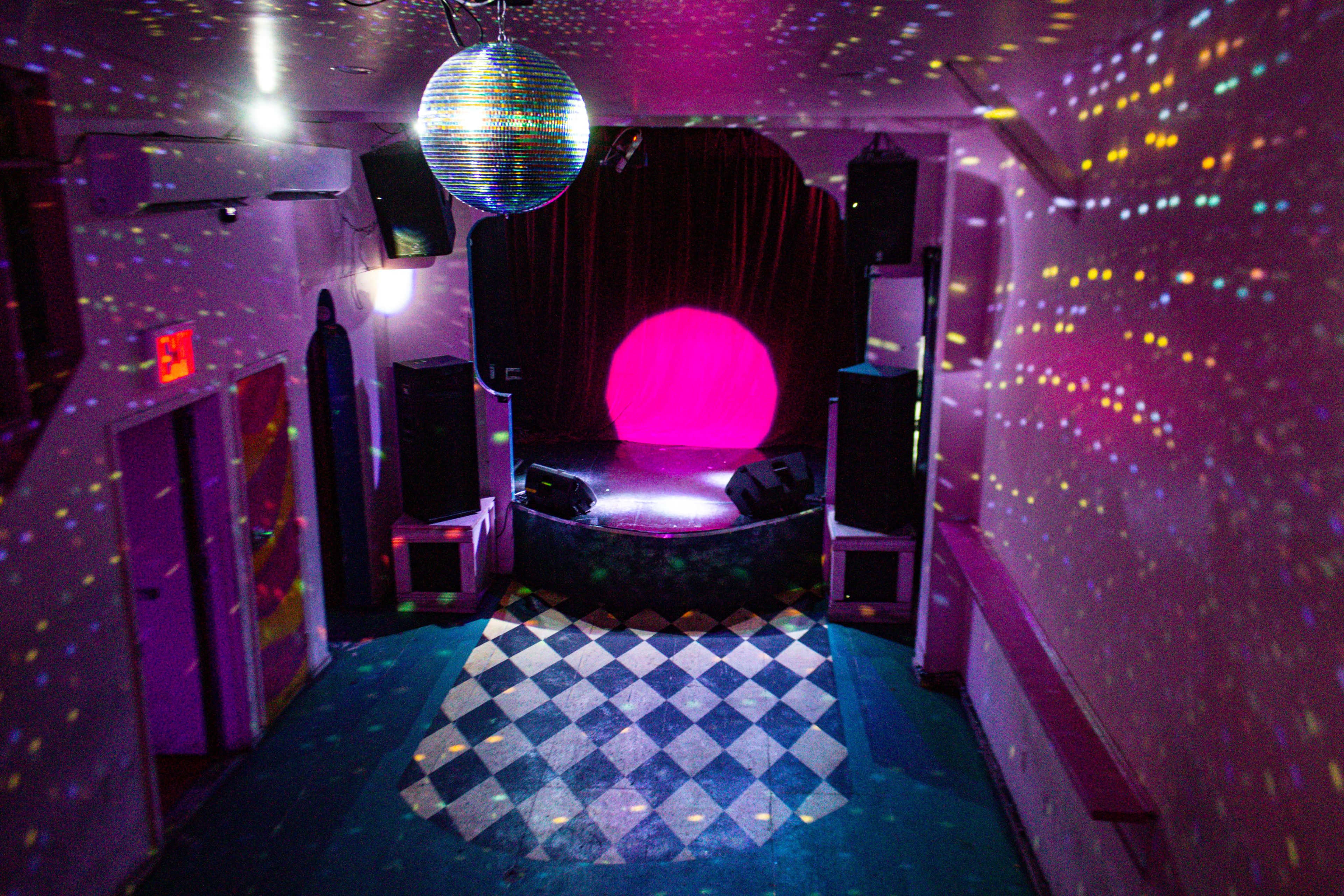 An empty performance space with a circular stage, colorful lights reflecting off the walls, and a disco ball hanging from the ceiling.
