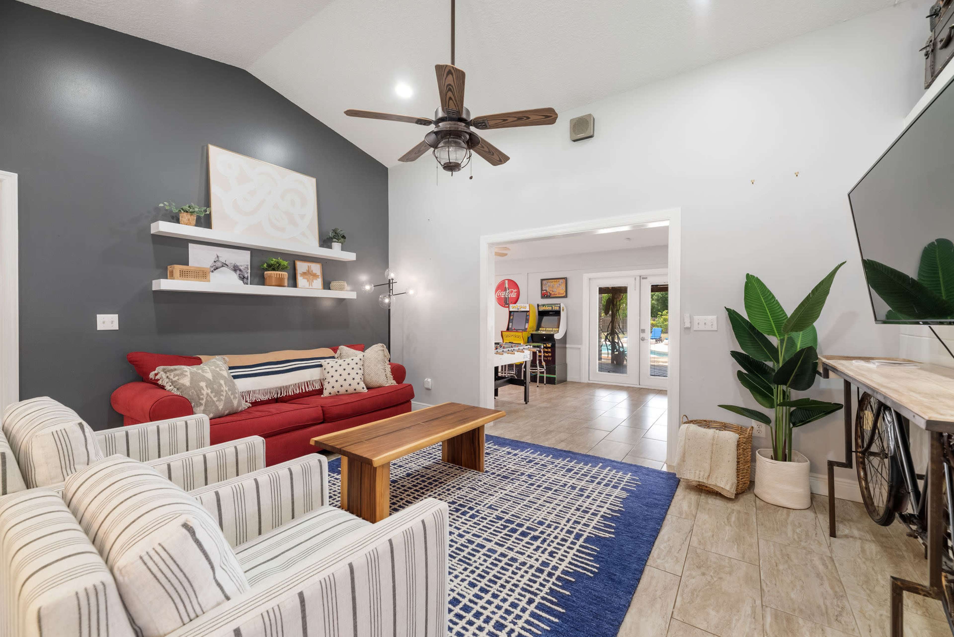 The living room features a red sofa, striped chairs, a wooden coffee table, and a view of an outdoor area through a doorway.