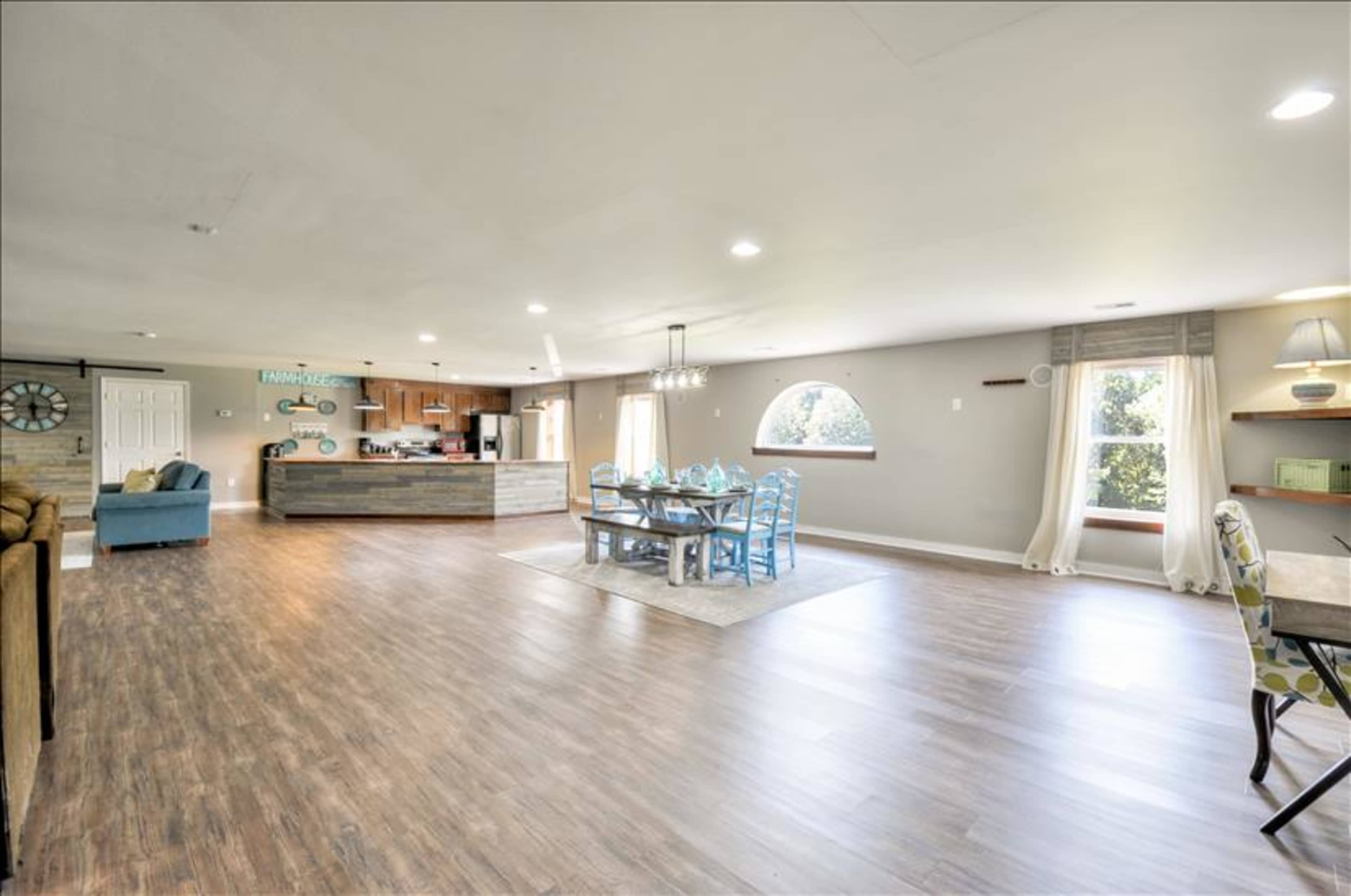 A spacious, open-concept living area features a dining table, a kitchen in the background, and large windows letting in natural light.