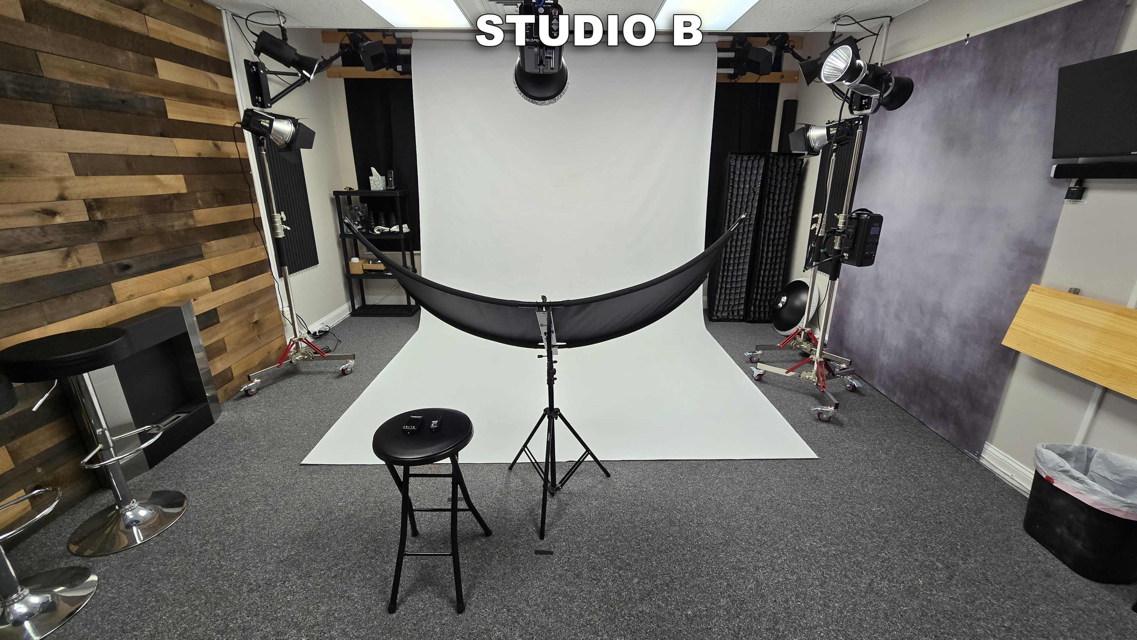 A photography studio with a white backdrop, a black fabric draped on a stand, and various lighting equipment arranged around the space.