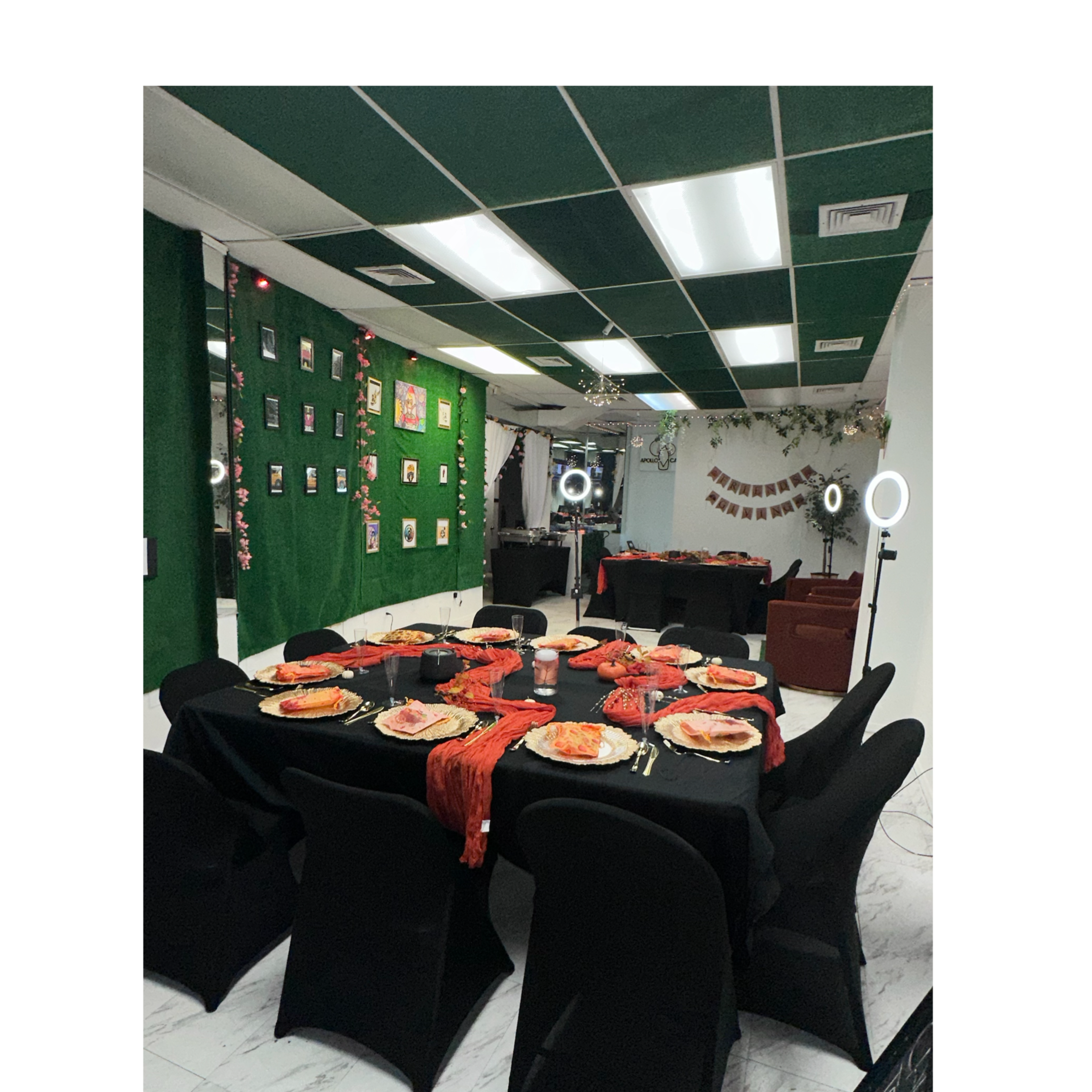 A dining area is set up with black tables and chairs, featuring red table settings and decorations, with photo displays on the wall.