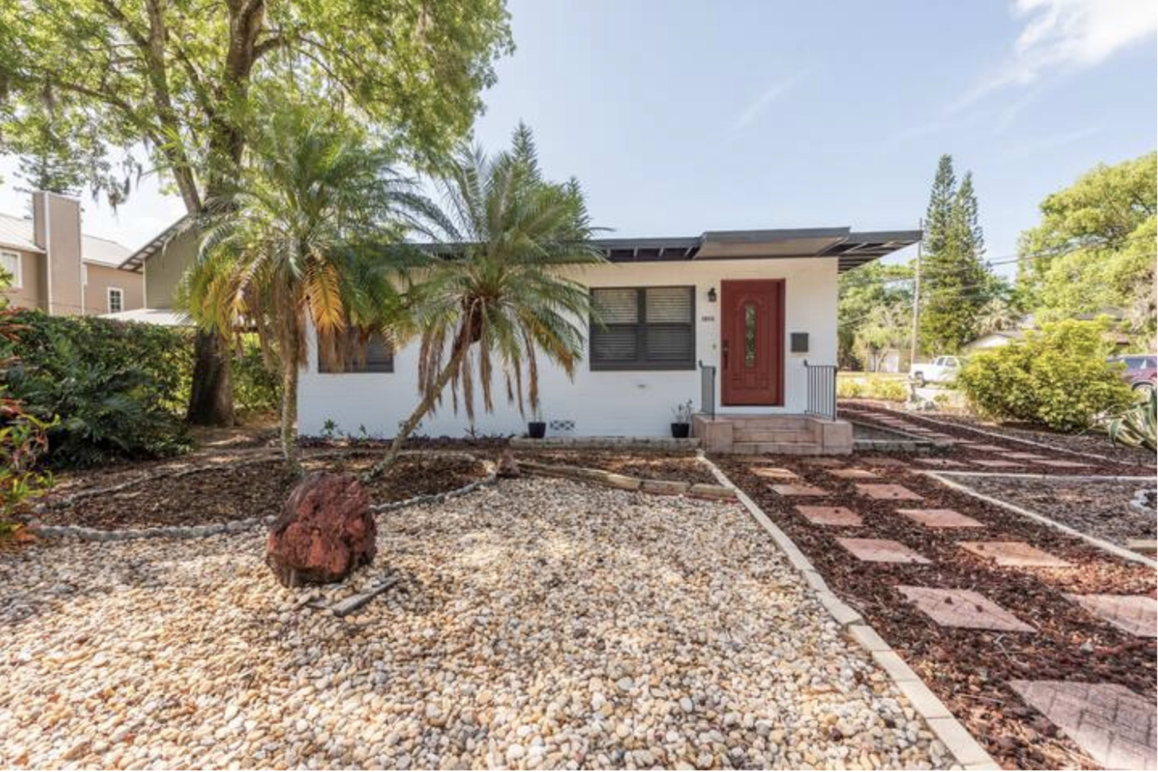 A single-story house with a red front door surrounded by landscaped gravel and greenery.