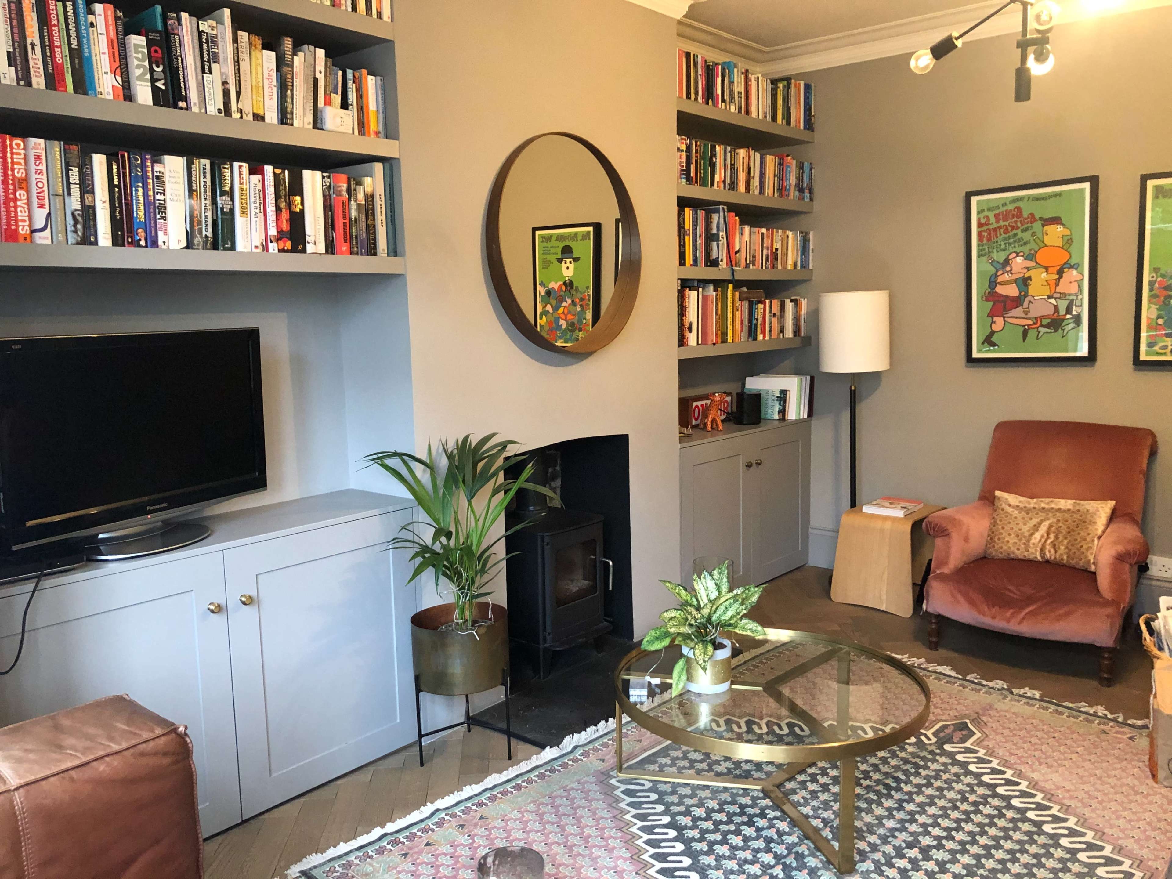 The image shows a cozy living room with bookshelves filled with books, a television, an armchair, a coffee table, and a decorative plant.