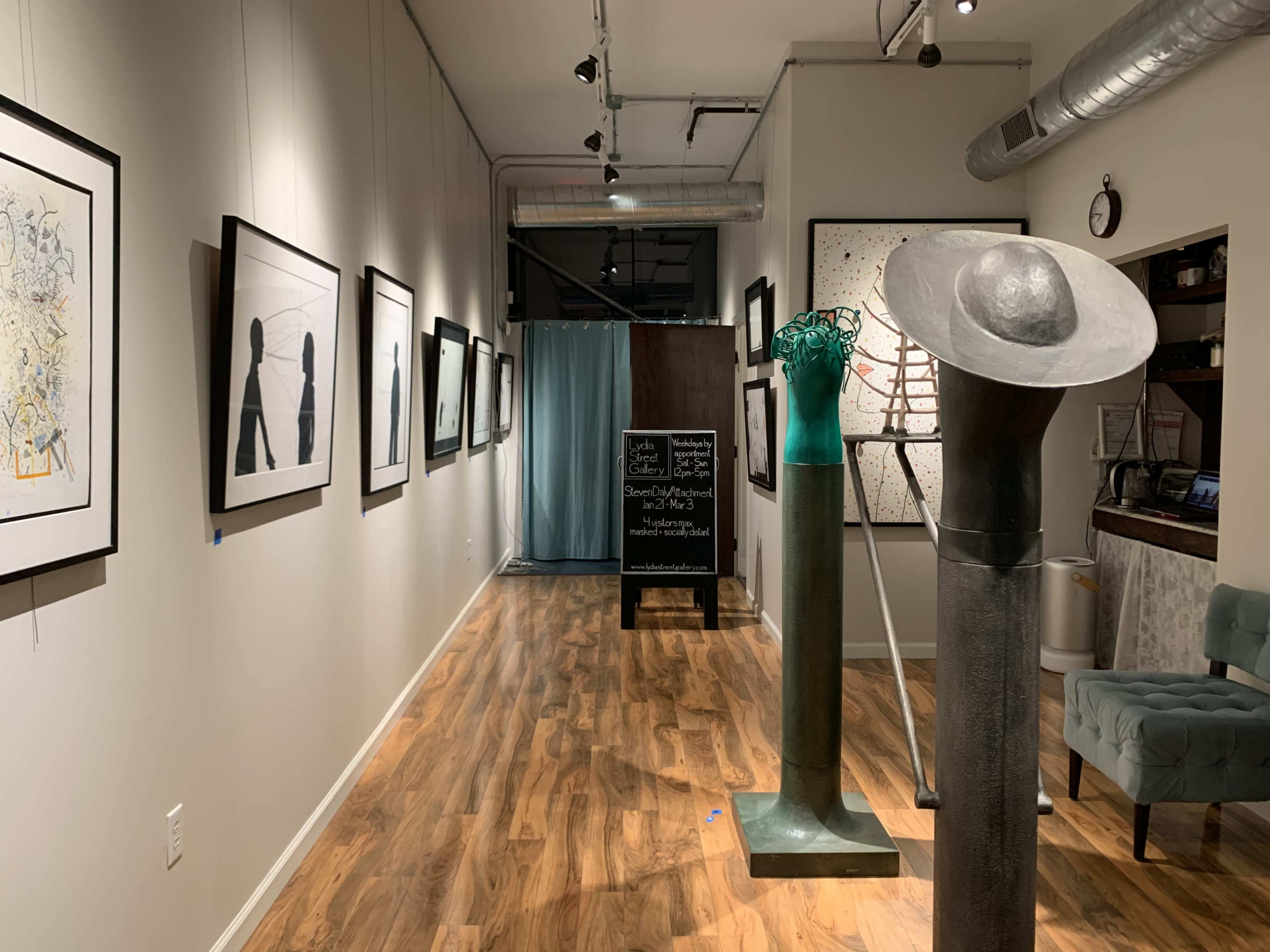 The image shows an art gallery corridor with framed artworks on the walls and sculptures displayed in the foreground.