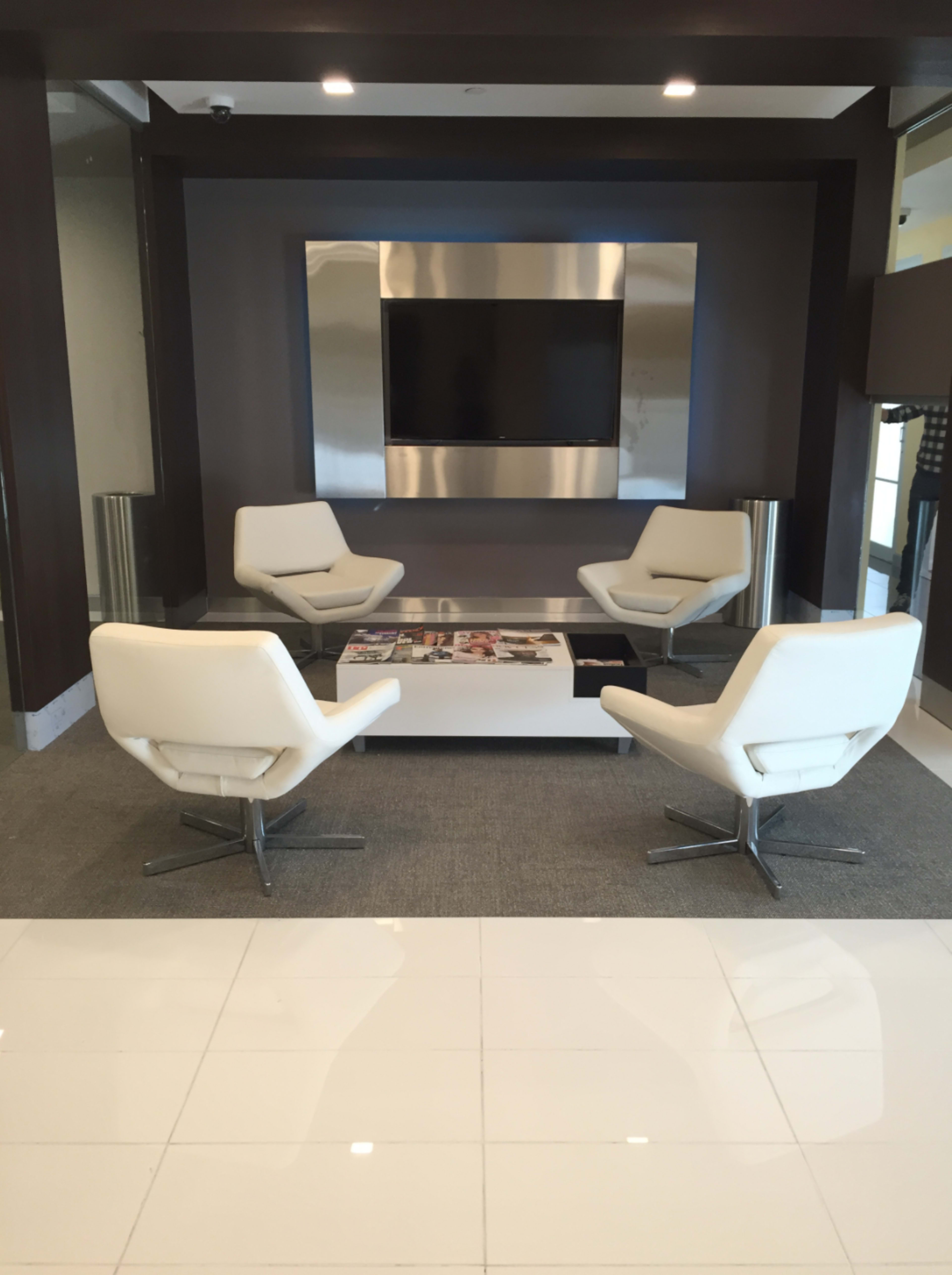 A modern sitting area features four white armchairs arranged around a low table in front of a wall-mounted television.