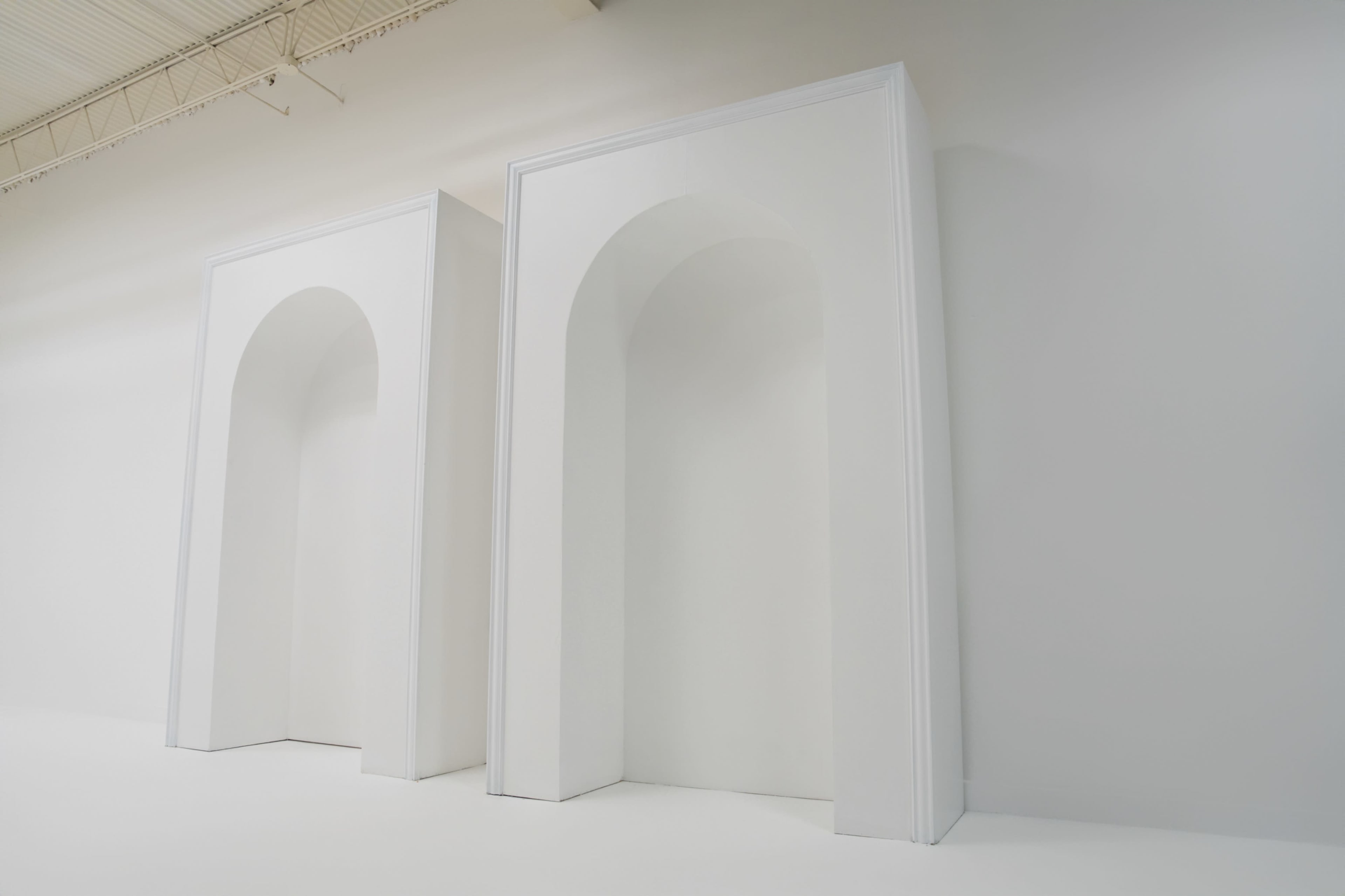 Two tall, white archways are set against a plain white wall in a well-lit space.