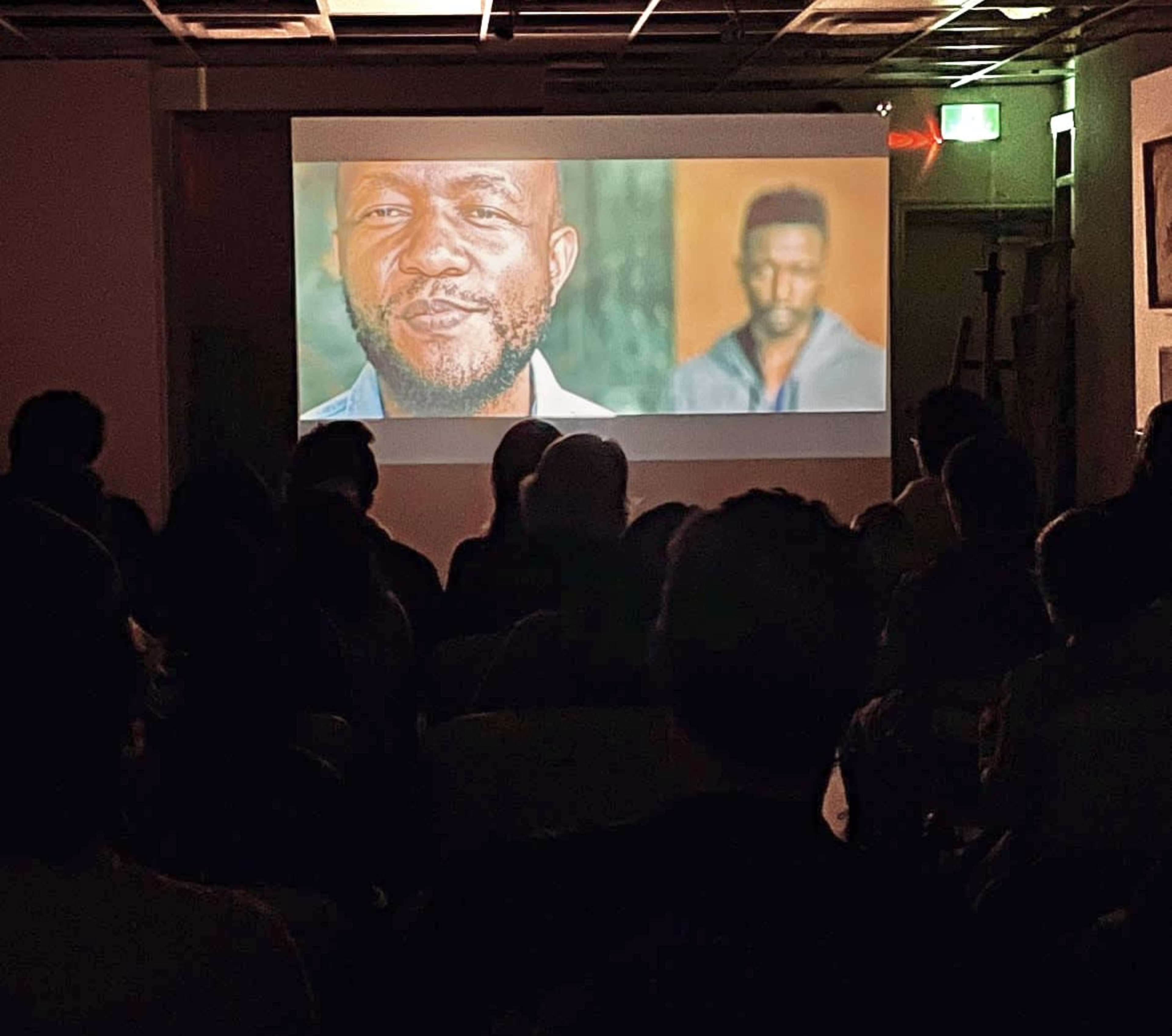 A crowd watches a large projected video on a screen in a dimly lit room.