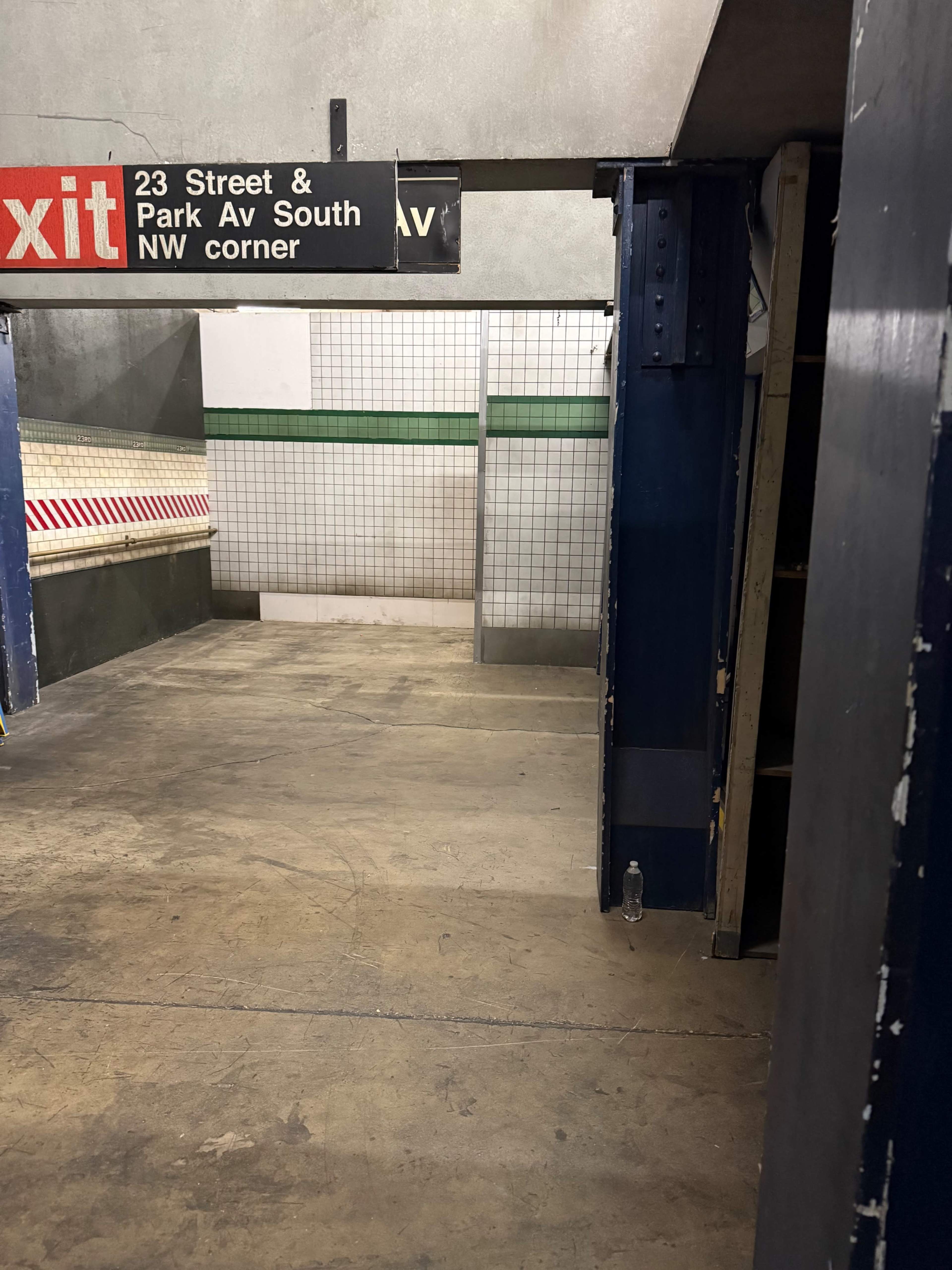The image shows a partially empty underground station corridor with an exit sign indicating "23 Street & Park Av South" and tiled walls.