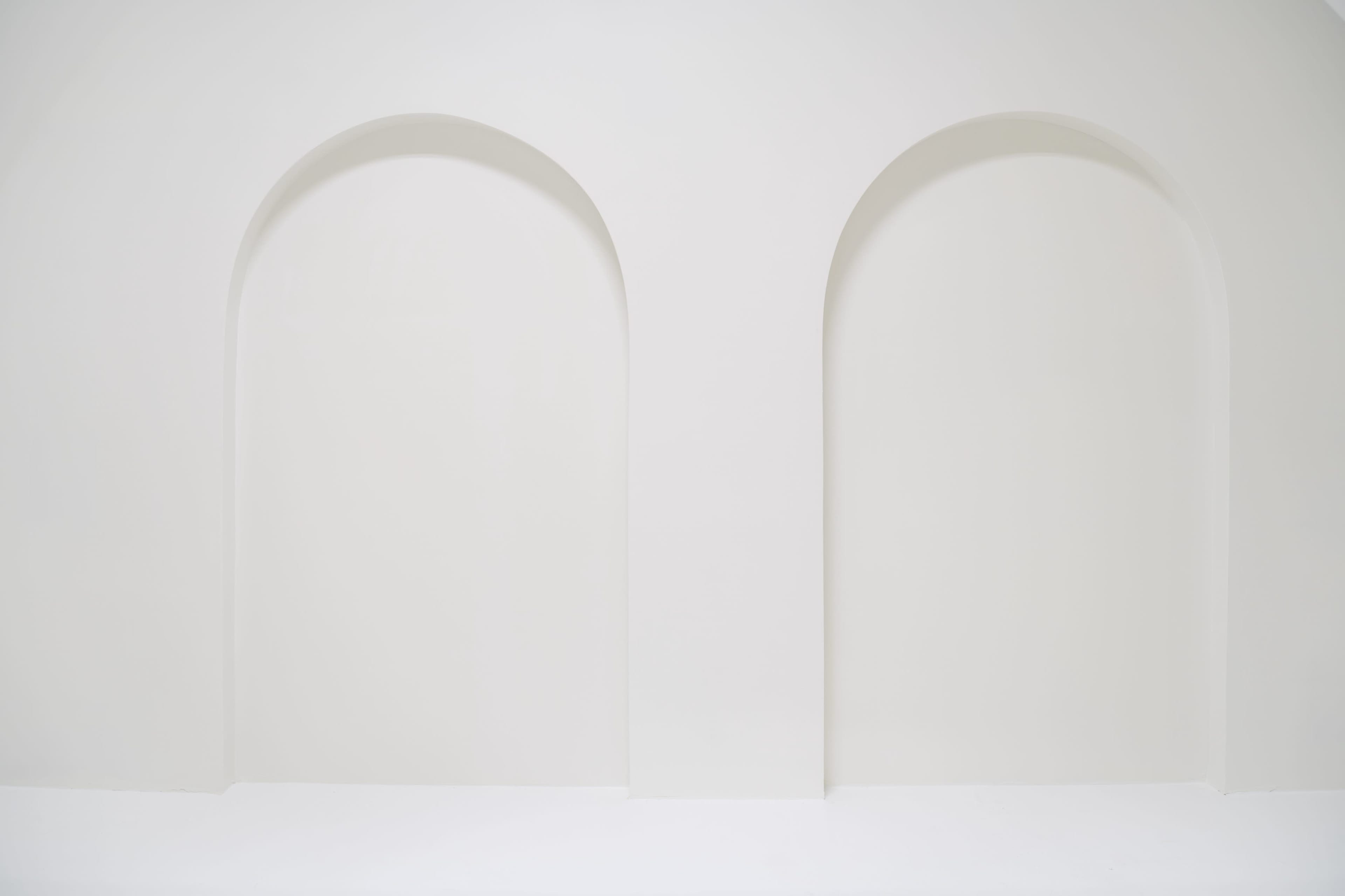The image features a minimalist white wall with two large, arch-shaped recesses.