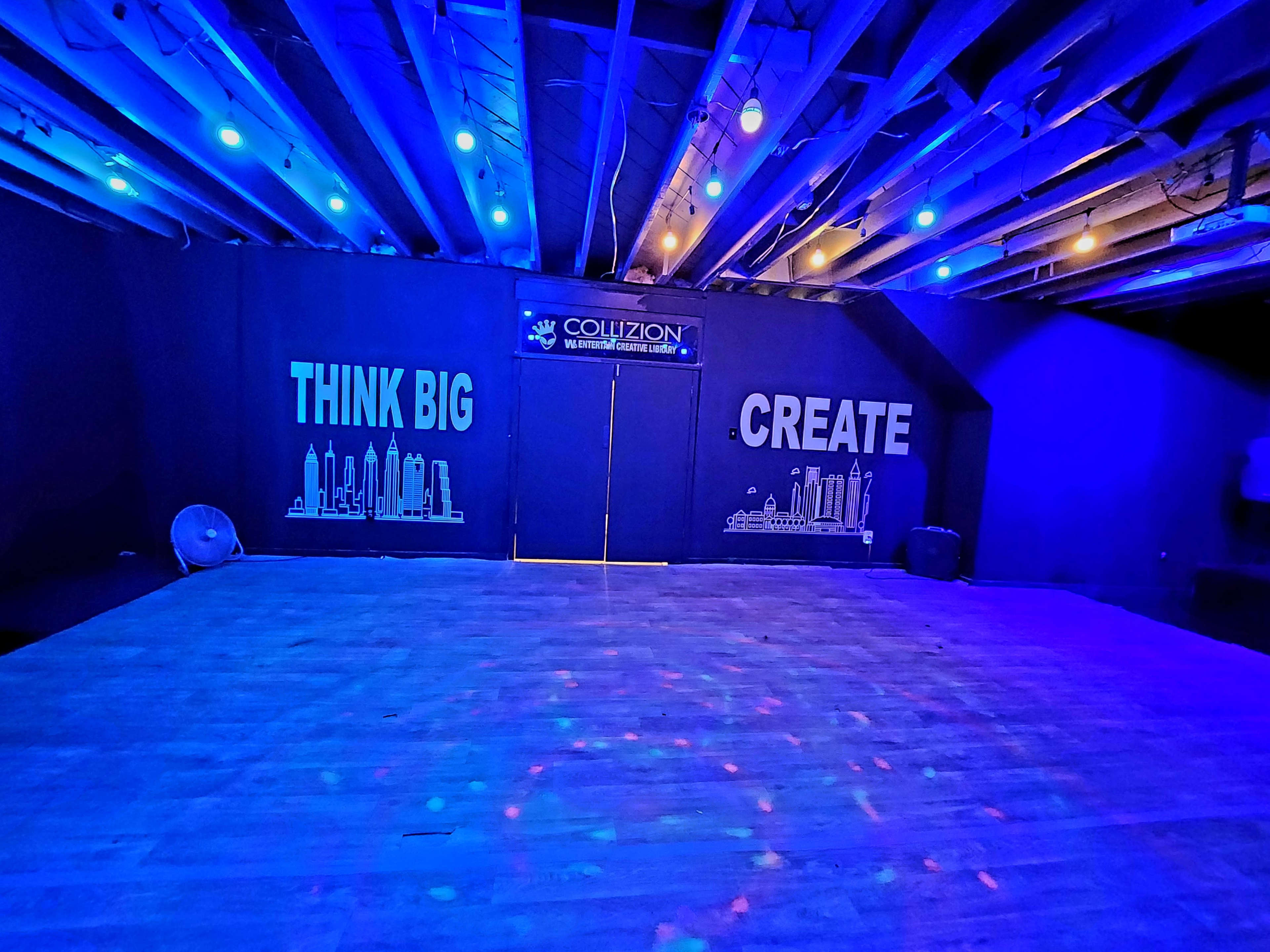 An empty dance or event space with blue lighting, featuring the phrases "THINK BIG" and "CREATE" on the walls.