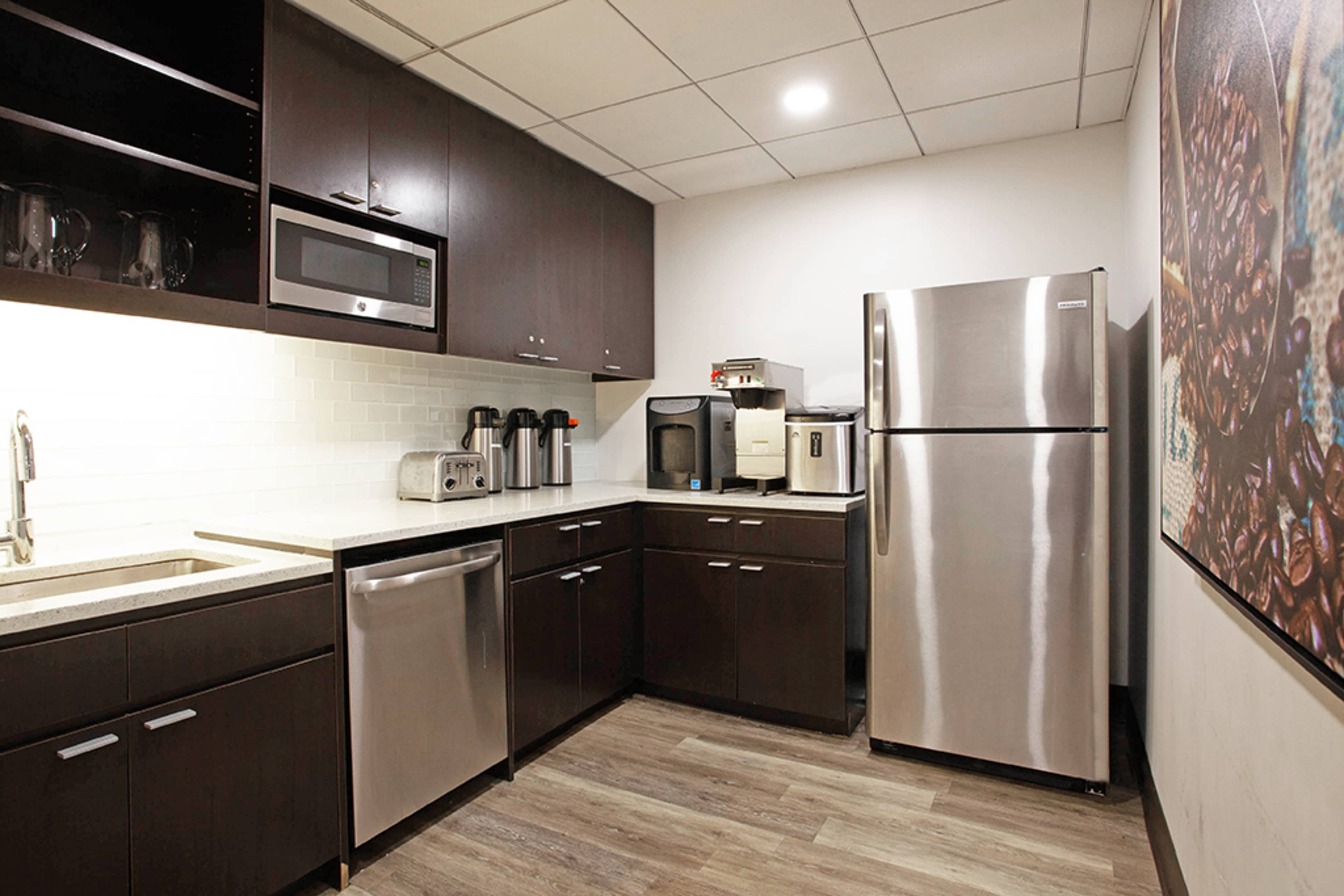 The image shows a modern kitchen area featuring dark cabinetry, stainless steel appliances, a double sink, and a countertop with various kitchen gadgets.