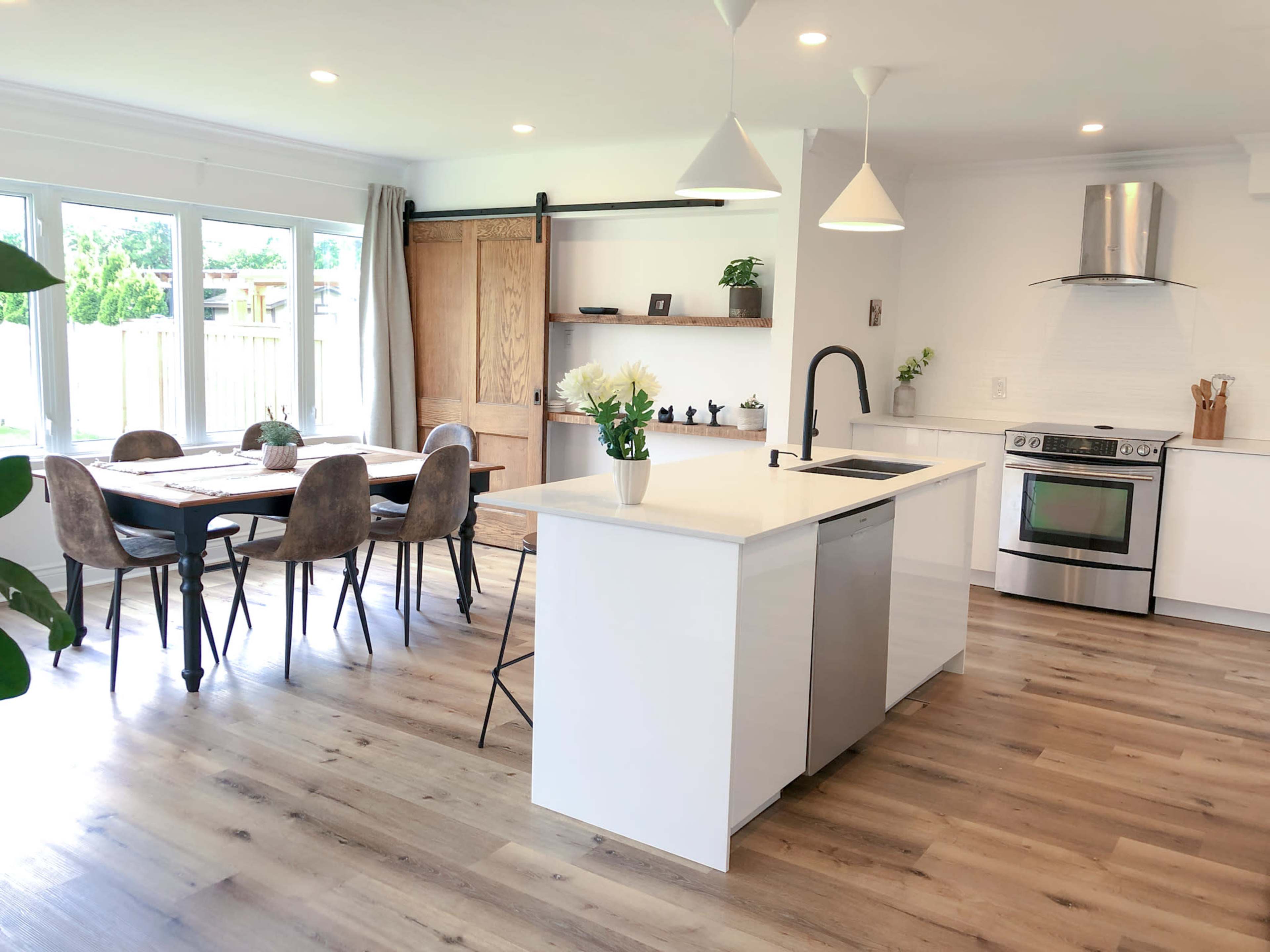 A modern kitchen and dining area with a large island, stainless steel appliances, and a wooden dining table surrounded by chairs.