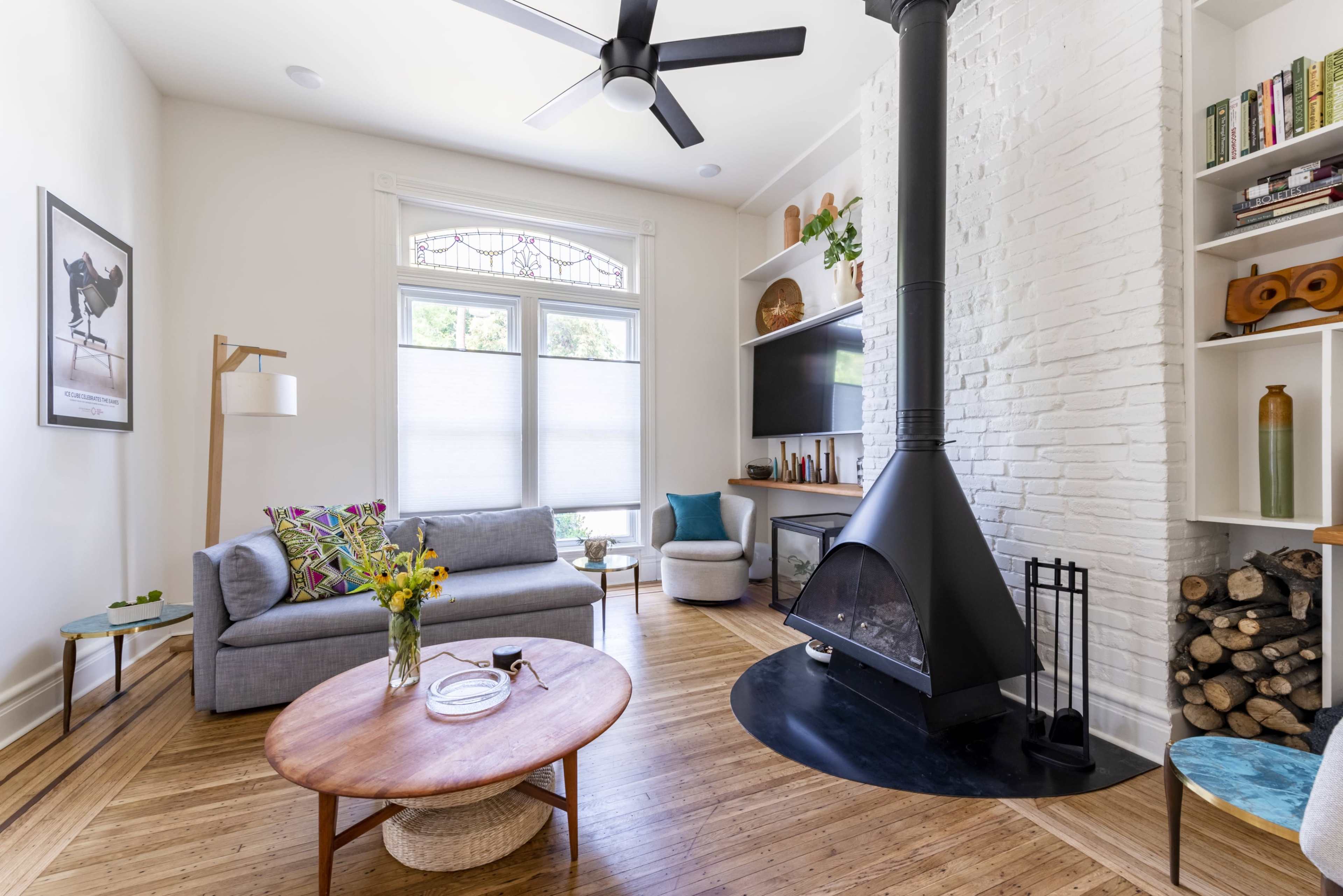 A modern living room featuring a gray sofa, a round wooden coffee table, and a black fireplace nestled against a white brick wall.