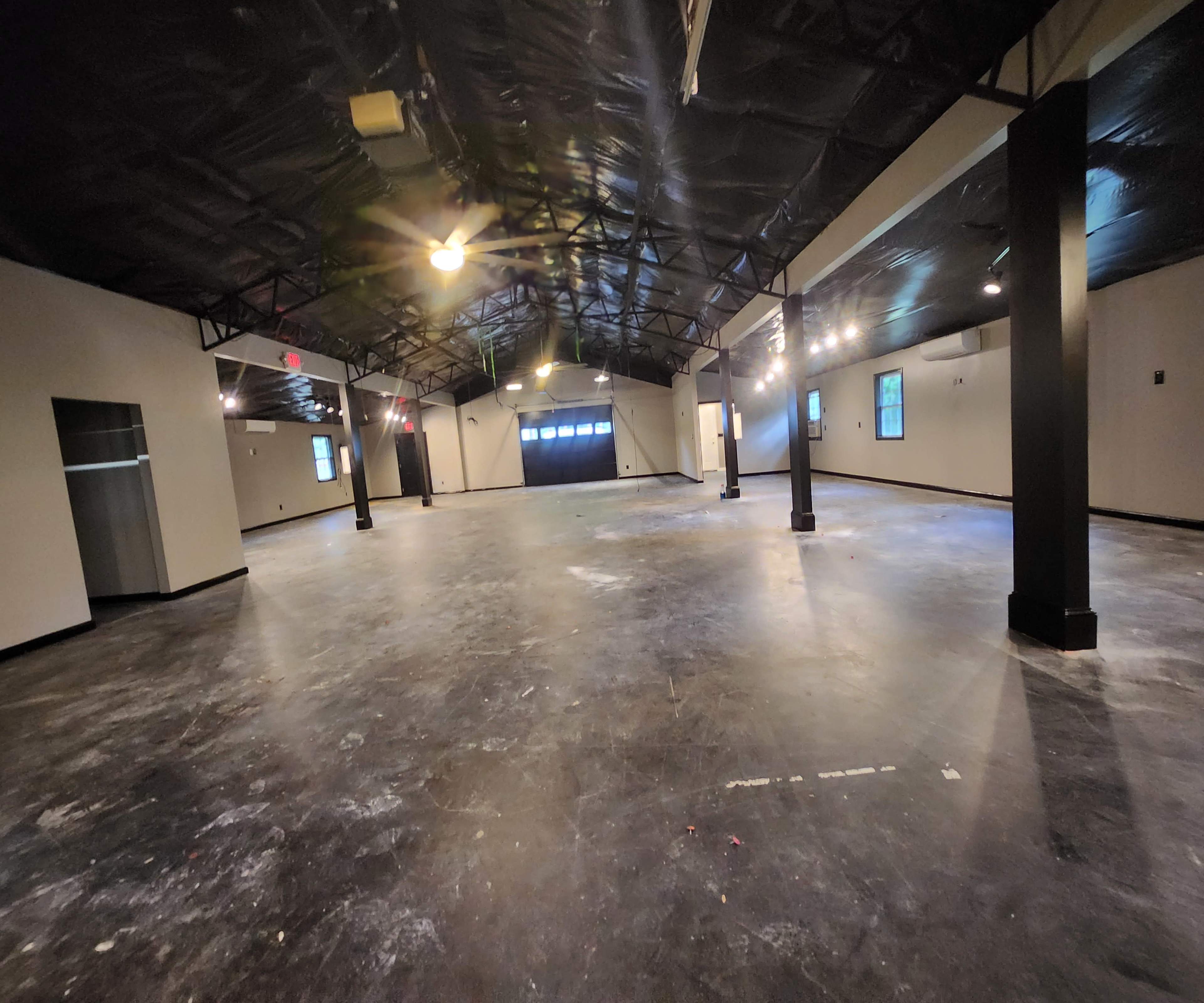 A spacious, empty interior of a building with a black ceiling, polished concrete floor, and several windows.