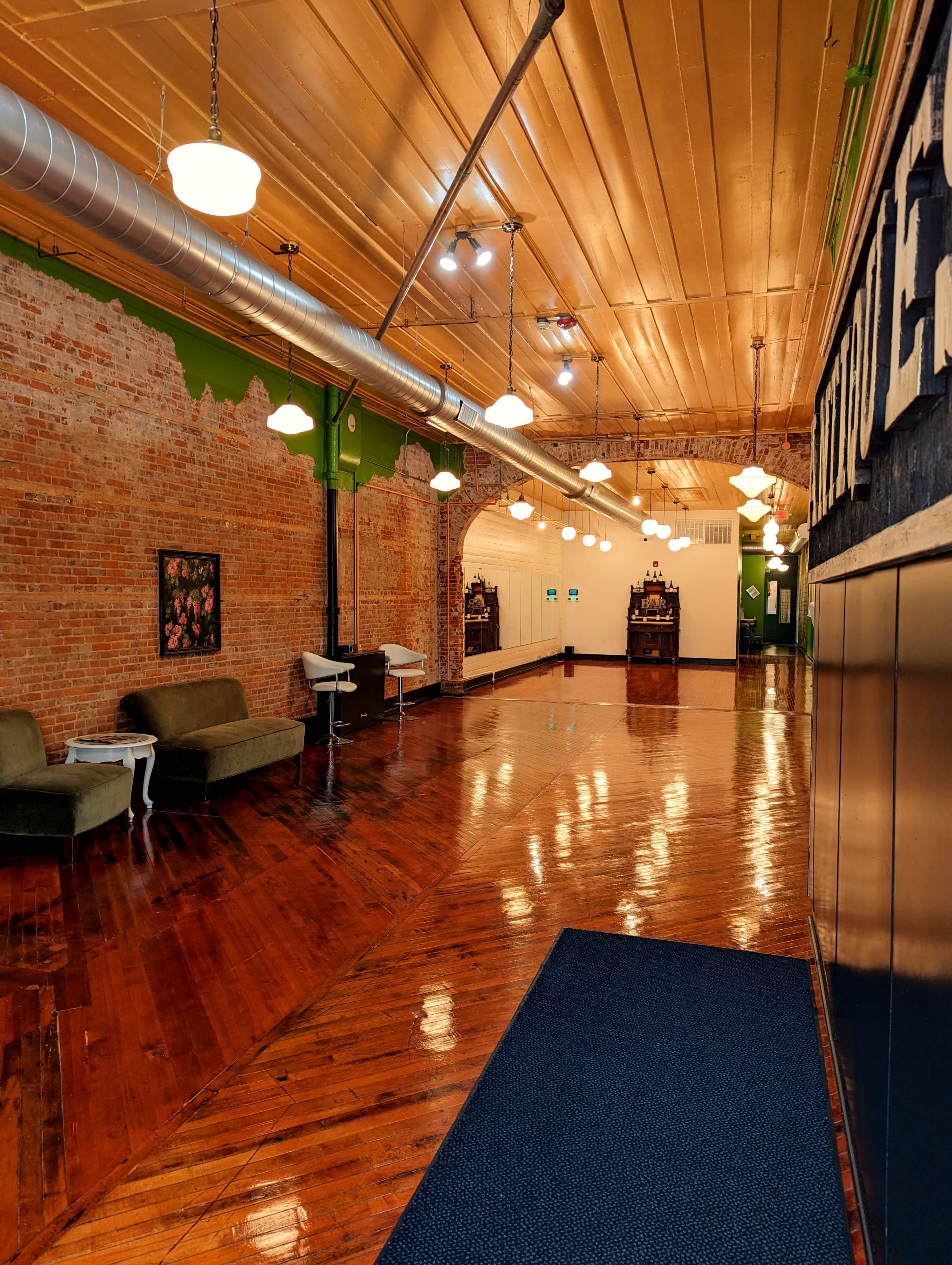 A spacious interior with hardwood floors, exposed brick walls, and a row of pendant lights illuminating the area.