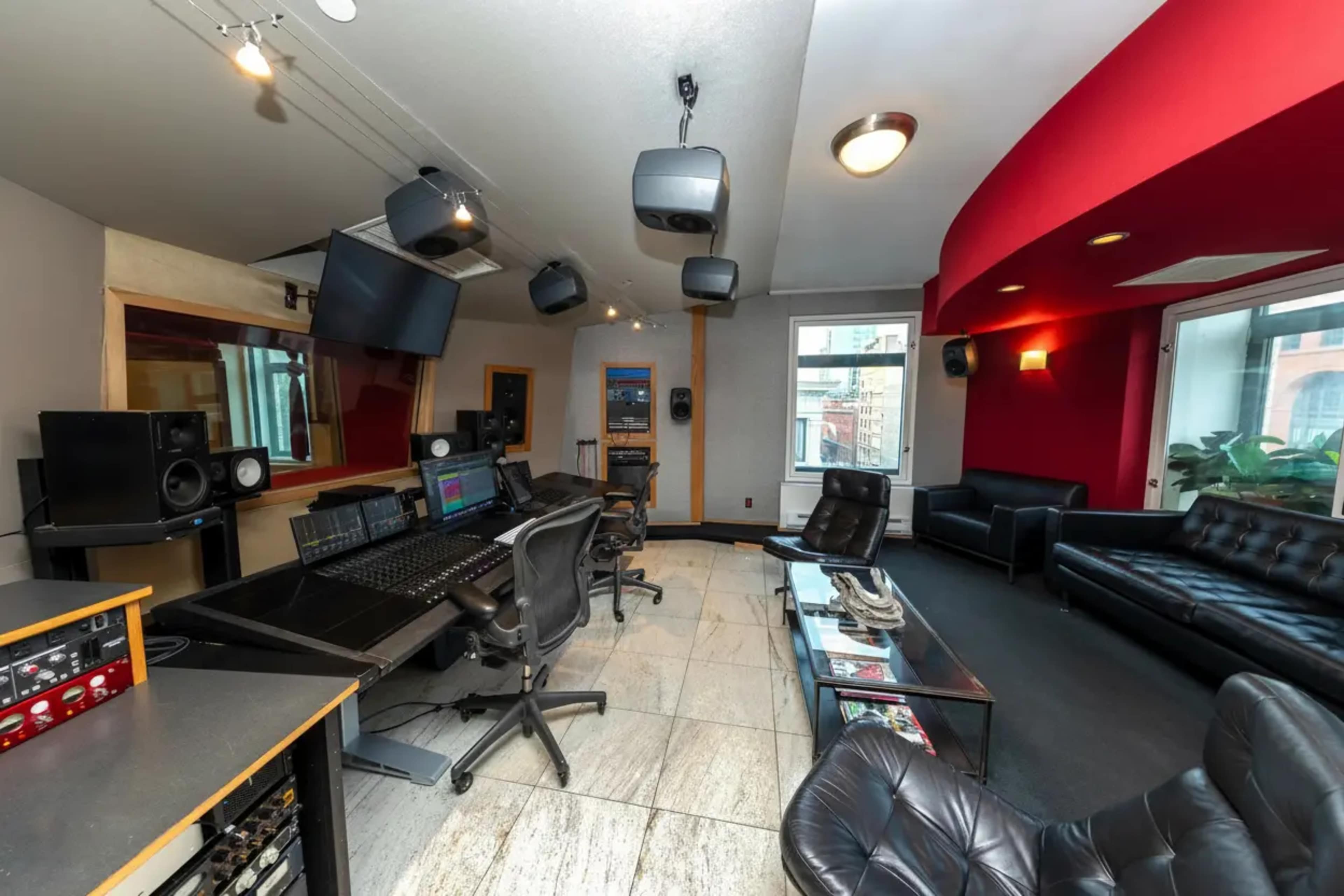 The image shows a music recording studio featuring a control desk, sound equipment, and seating areas with leather chairs and a sofa.