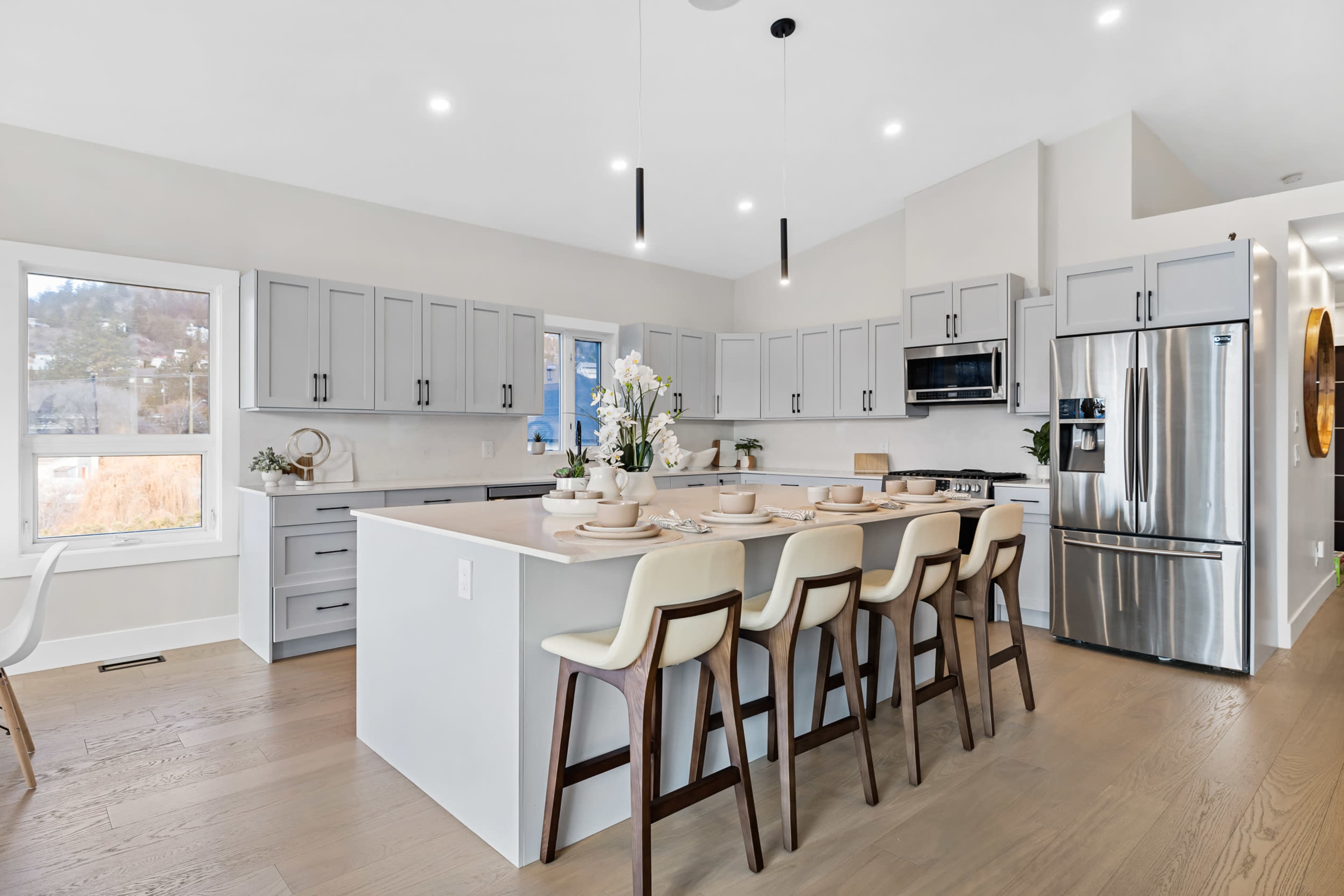 A modern kitchen features a large central island with seating, gray cabinets, and stainless steel appliances.