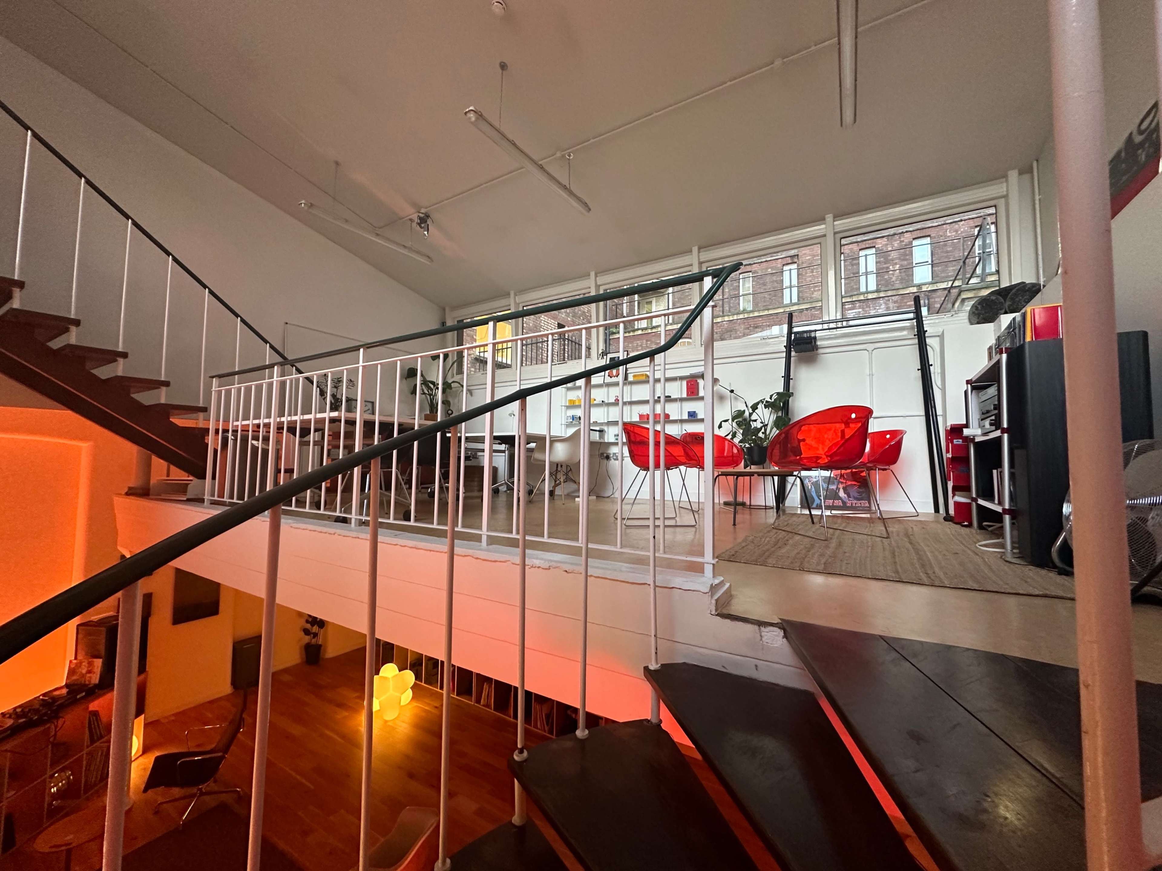 A modern, open-plan space featuring a staircase leading to a loft area with red chairs and a bookshelf.