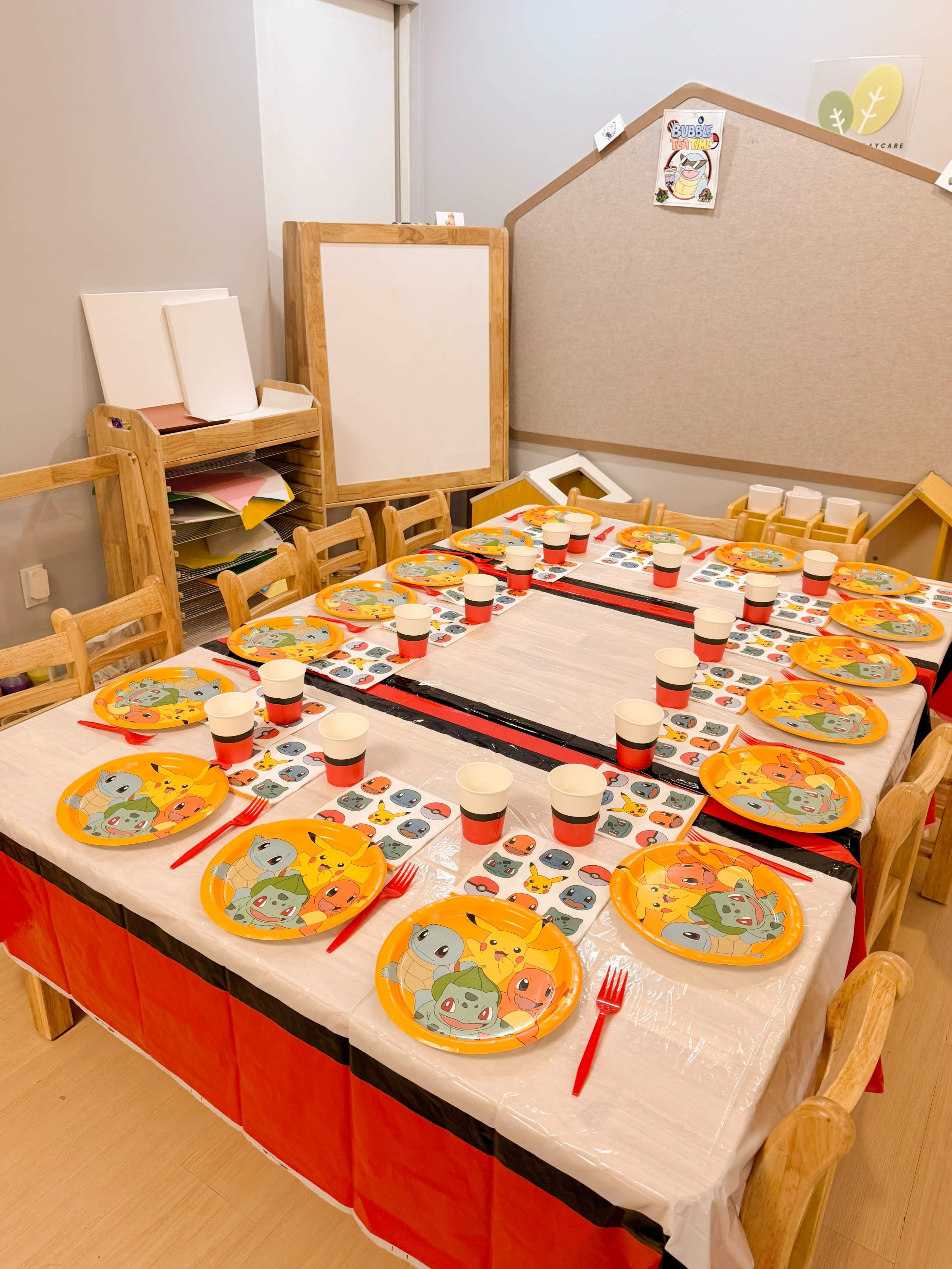 A table is set with colorful plates and cups, surrounded by wooden chairs in a decorated room.