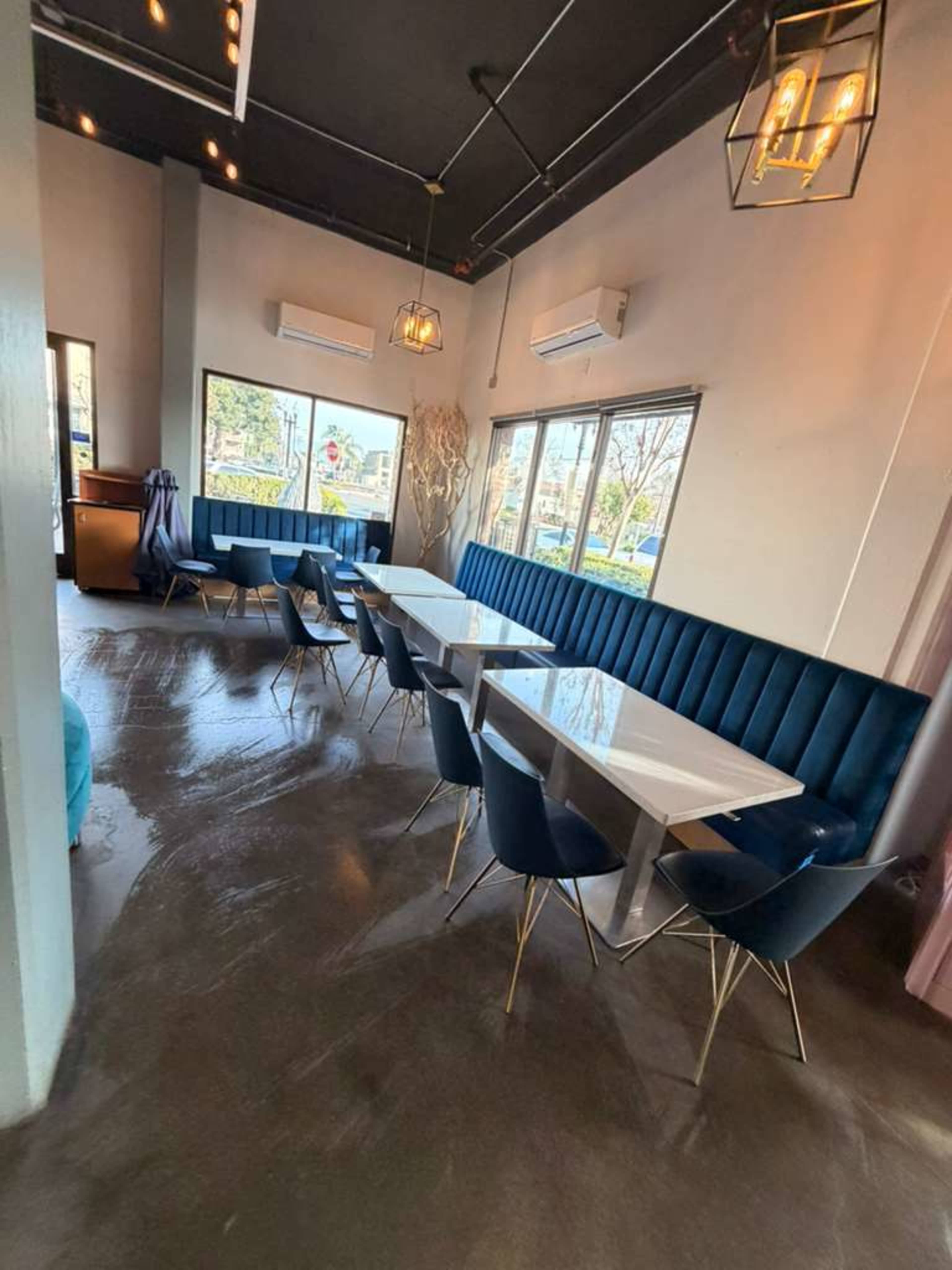 The image shows a modern restaurant interior with blue upholstered seating and white marble tables arranged in a well-lit space with large windows.