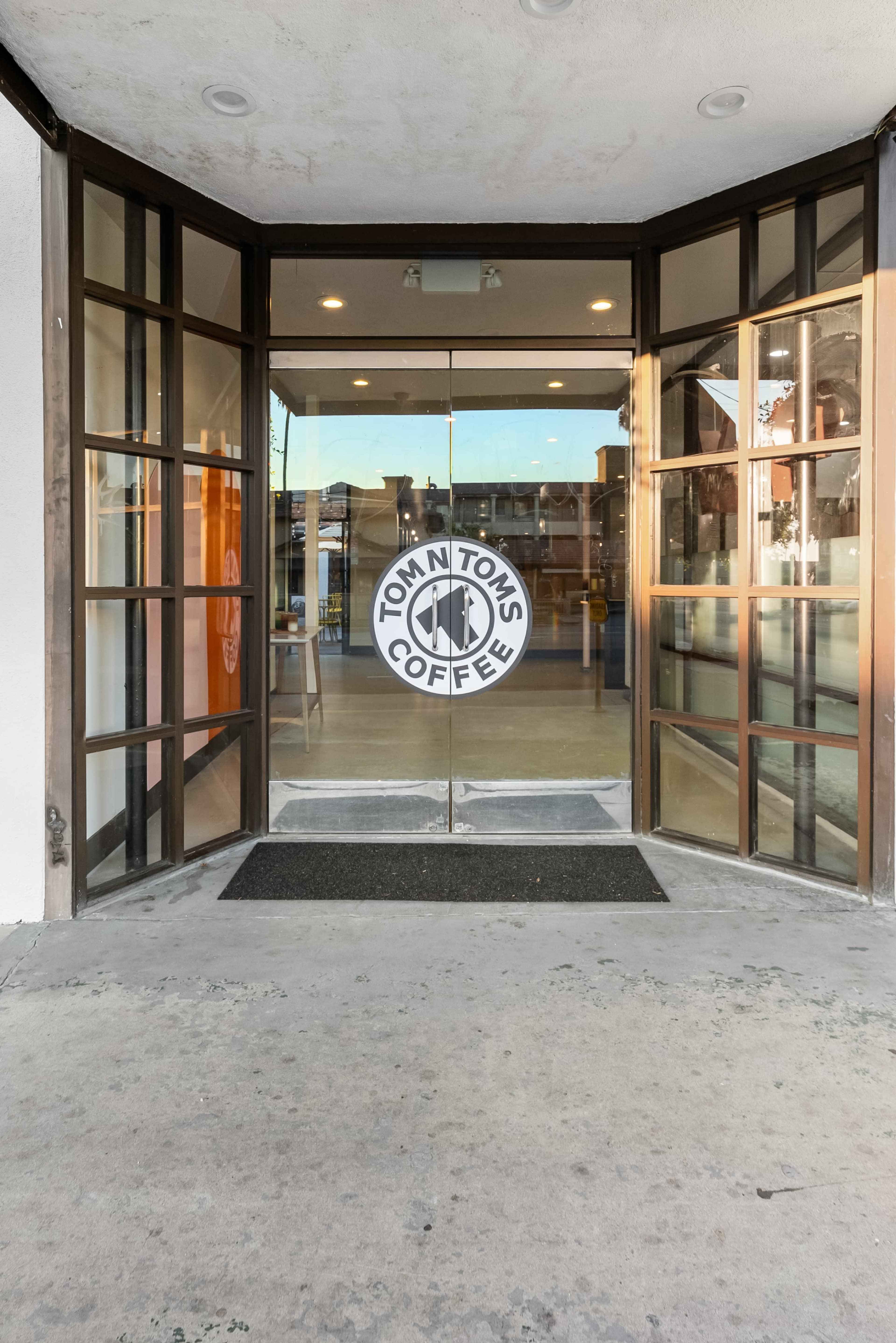 The entrance of a coffee shop with glass double doors featuring a round logo that reads "Tom N Toms Coffee."