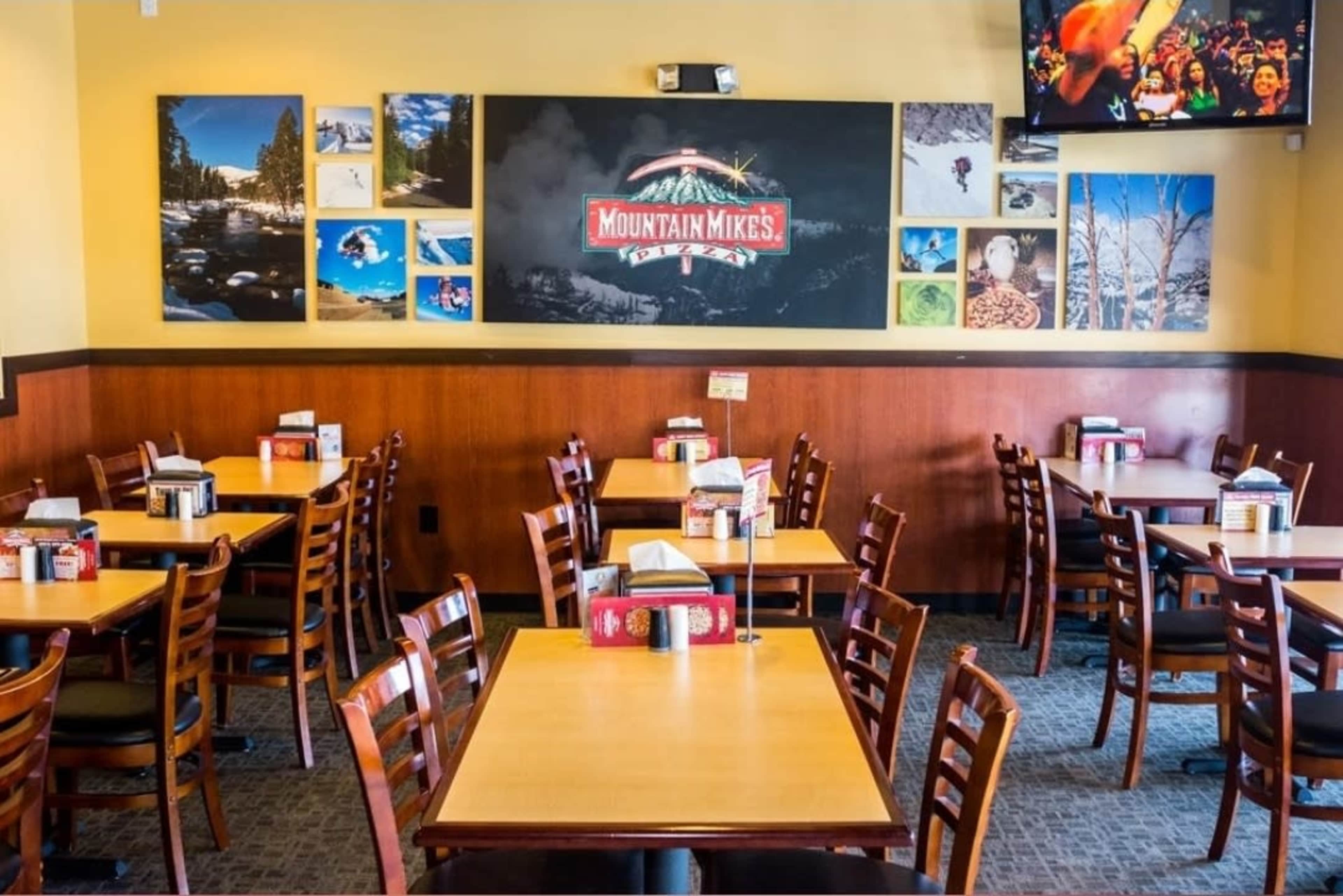 The image shows the interior of a casual dining restaurant with wooden tables and chairs, and a wall featuring photographs of outdoor scenes.