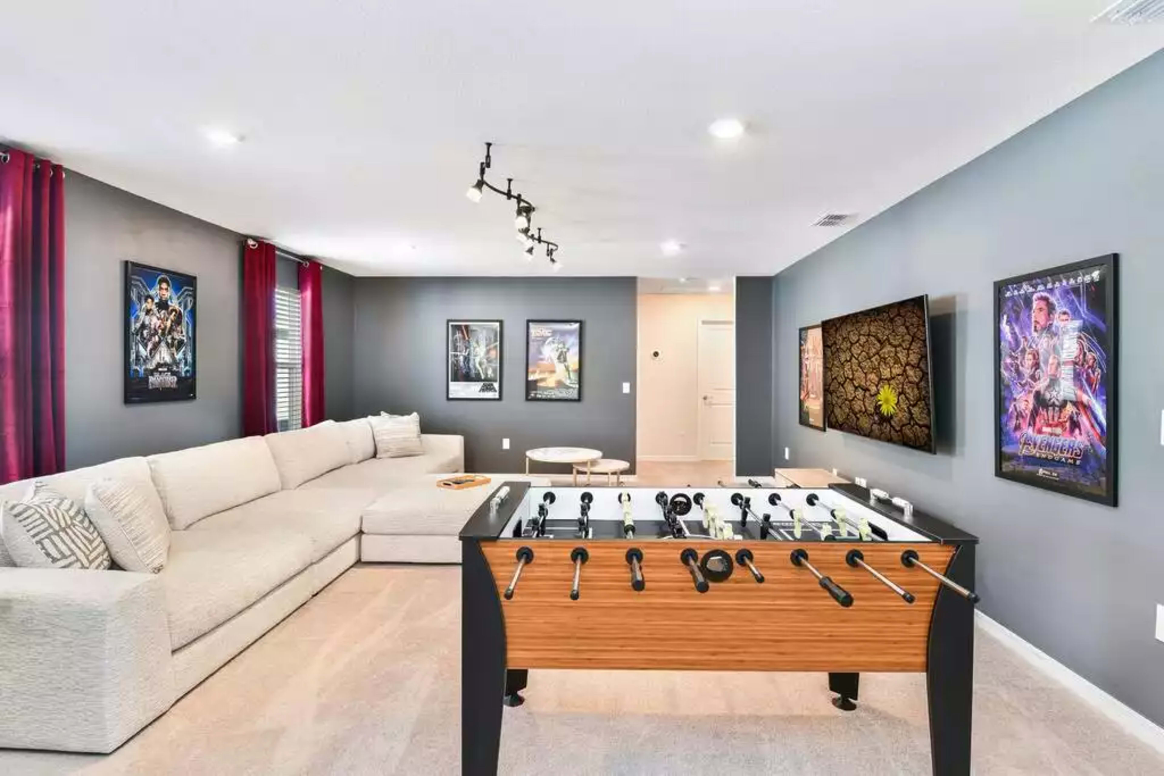 A game room featuring a large sectional couch, a foosball table, and movie posters on the walls.