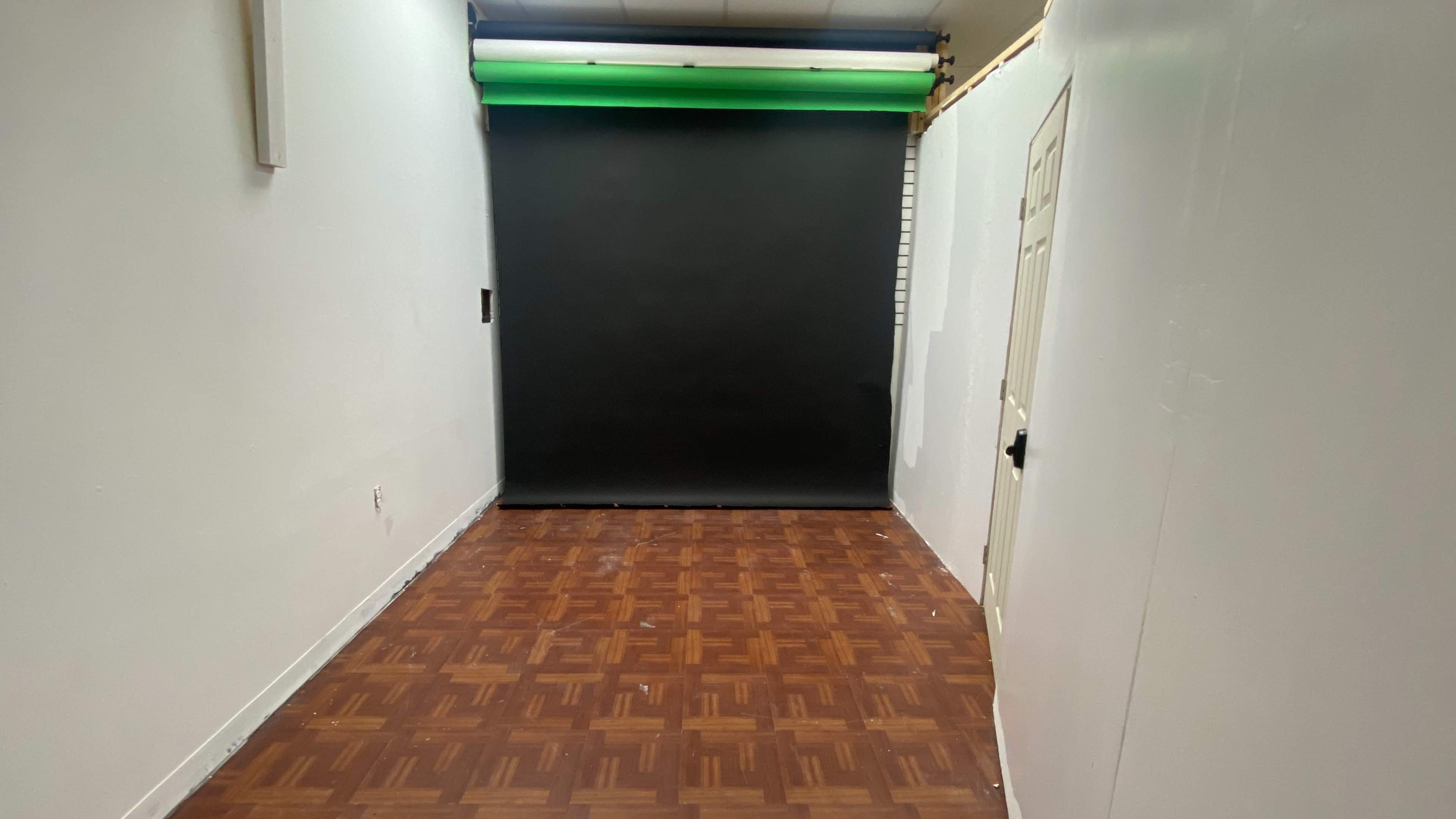 A sparsely furnished room with a wooden floor and a dark backdrop at one end.