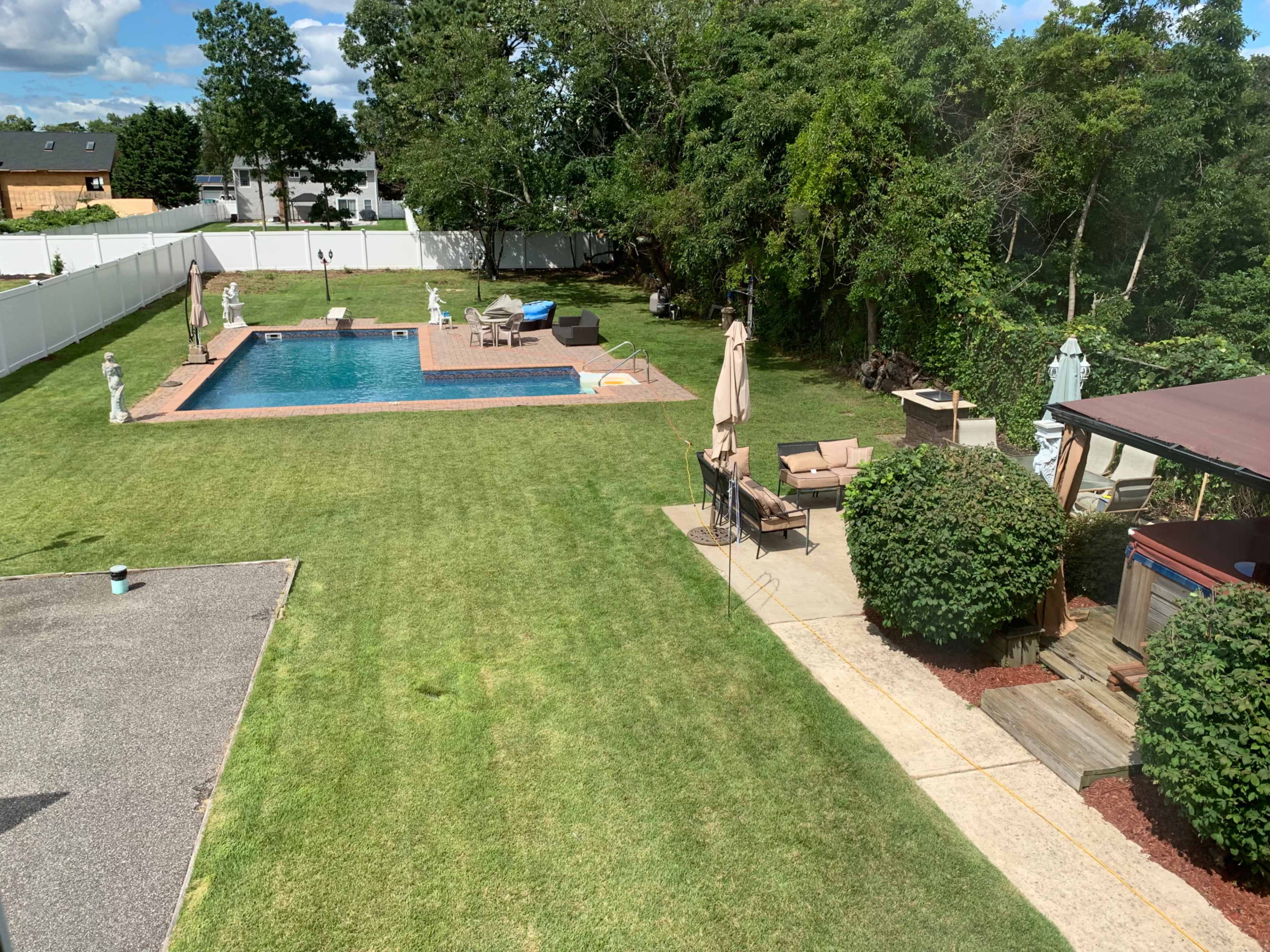 A backyard with a swimming pool, landscaped grass, garden furniture, and decorative statues.